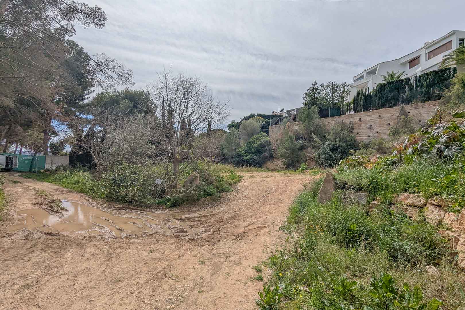 Verhoogd bouwperceel in La Corona, met het natuurlijke terrein omgeven door mediterrane vegetatie en nabijgelegen villa's op de heuvel.