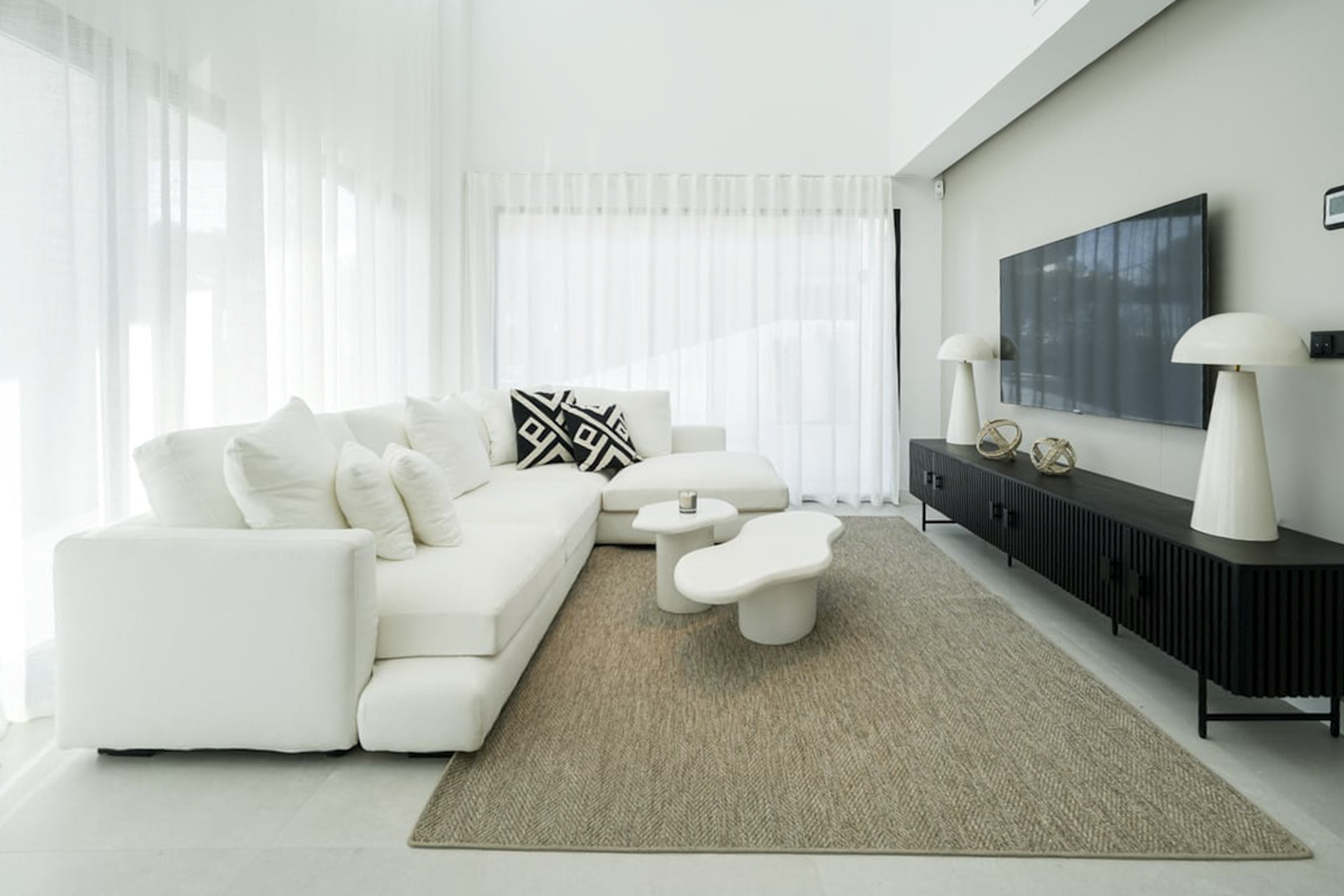Lichte woonkamer met modulaire witte bank, moderne bijzettafel en jute vloerkleed.