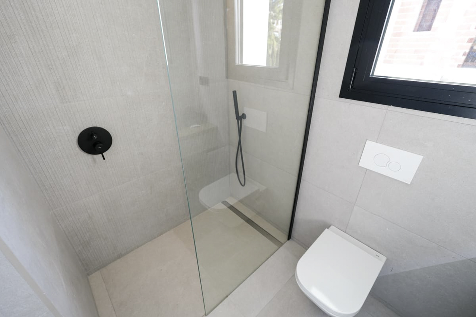 Modern badkamerdetail met glazen douche, zwarte armaturen en grijze tegels met textuur.