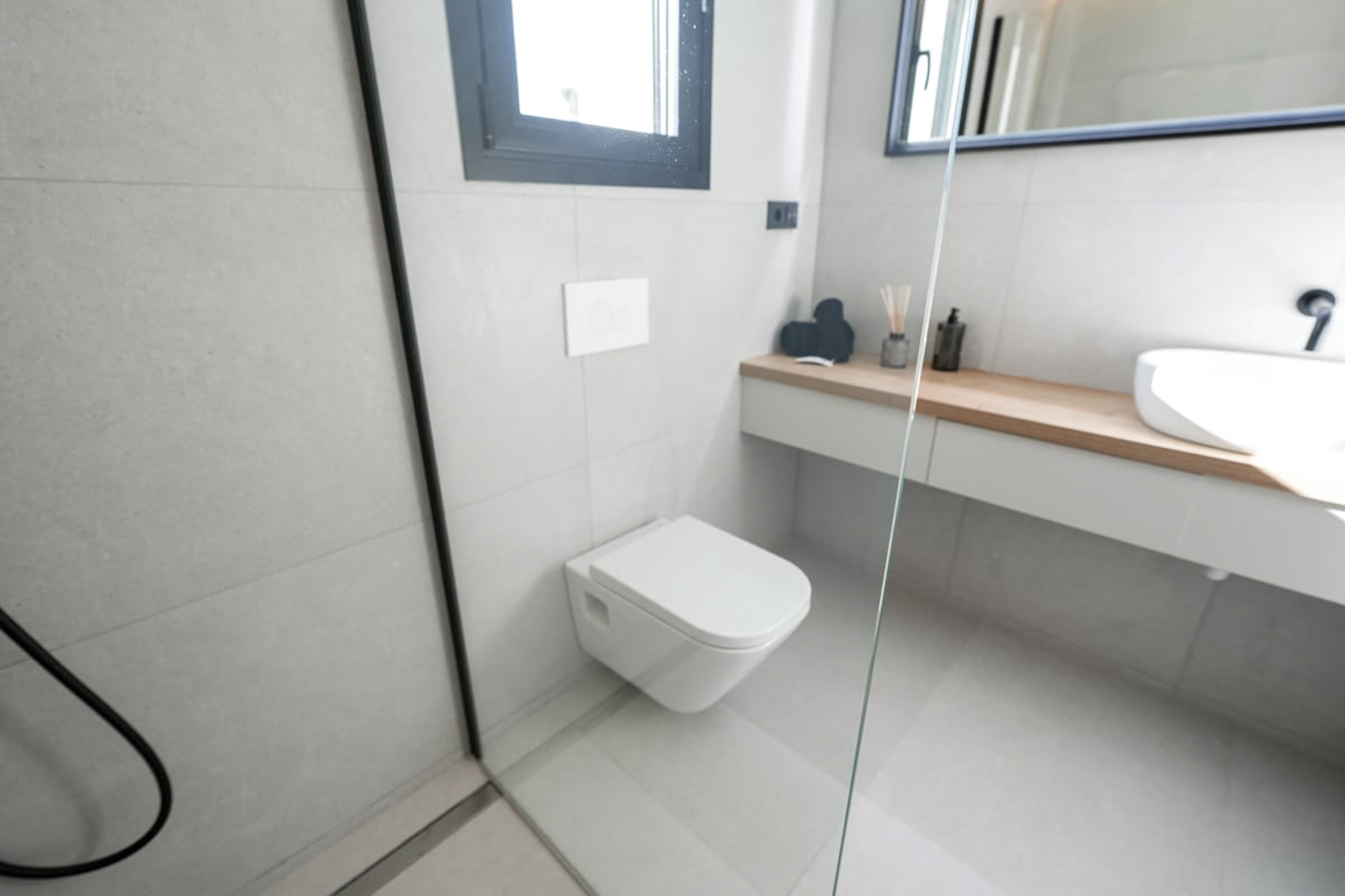 Modern badkamerdetail met grijze tegels, een hangend toilet en een licht houten aanrecht.