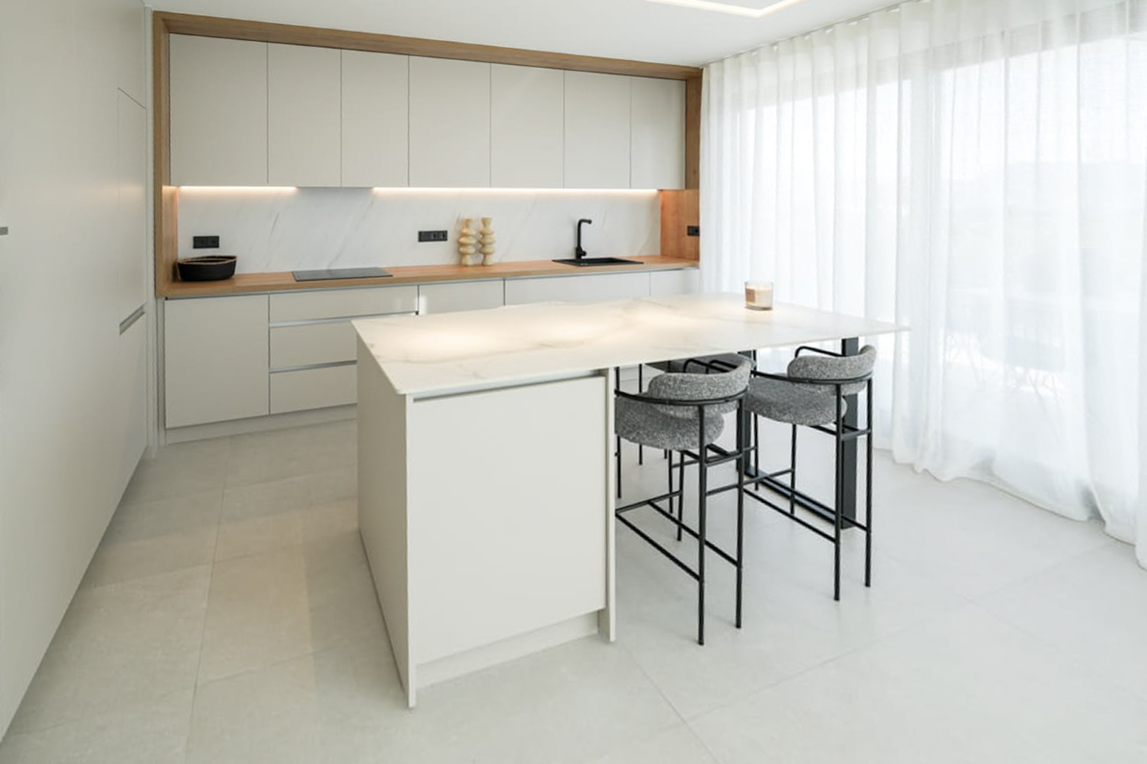 Moderne keuken met marmeren eiland, grijze krukken en witte kasten onder natuurlijk licht.