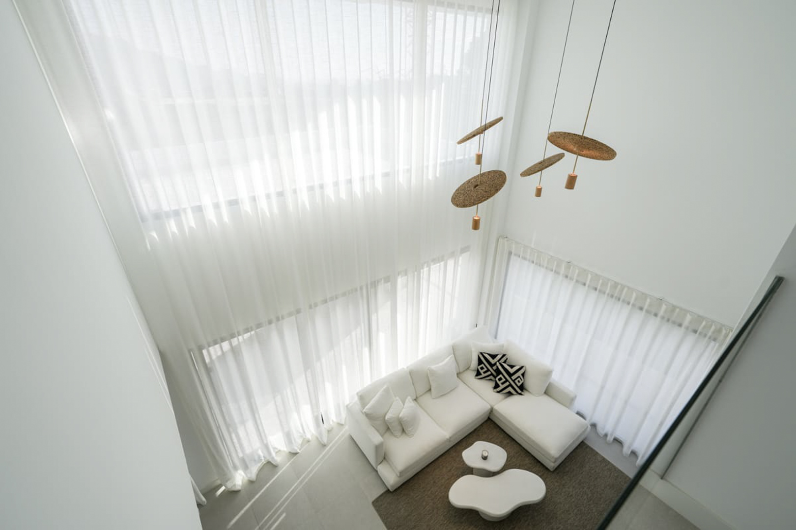 Verhoogd zicht op de woonkamer met witte gordijnen, een modulaire bank en design hanglampen.