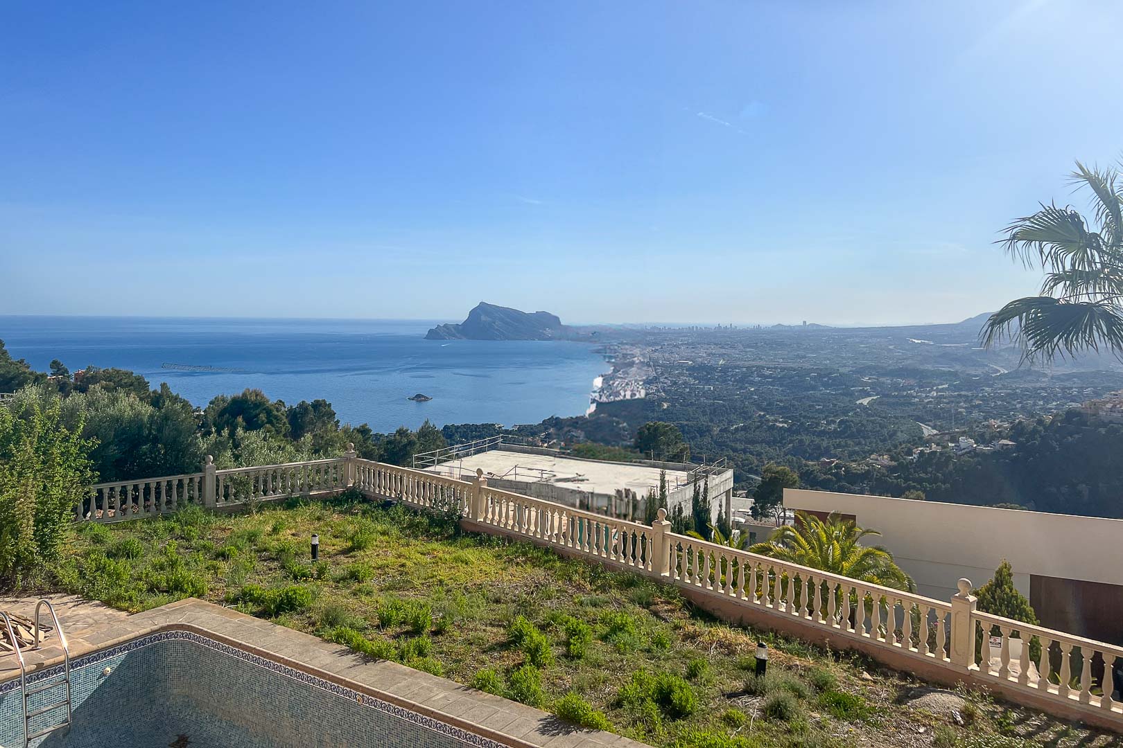 Panoramisch uitzicht op de Middellandse Zee en de Peñón de Ifach vanaf de buitenruimte met stenen balustrade en tuin.