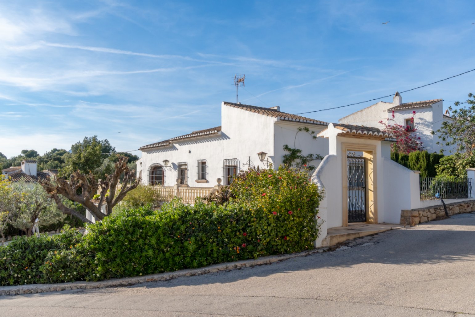 Mediterrane gevel met witte muren, smeedijzeren raamroosters en een voetgangersingang omlijst met traditionele Tosca-natuursteen.