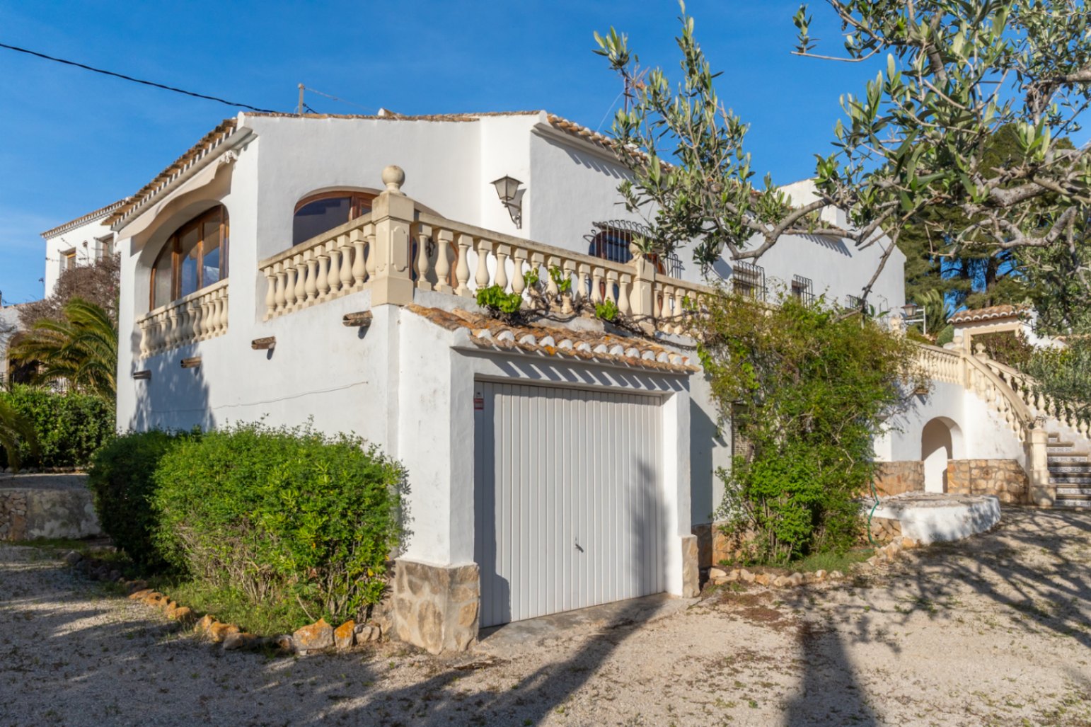 Mediterrane witte gevel met geïntegreerde garage, traditionele stenen balustrade en een buitentrap versierd met decoratieve keramische tegels.