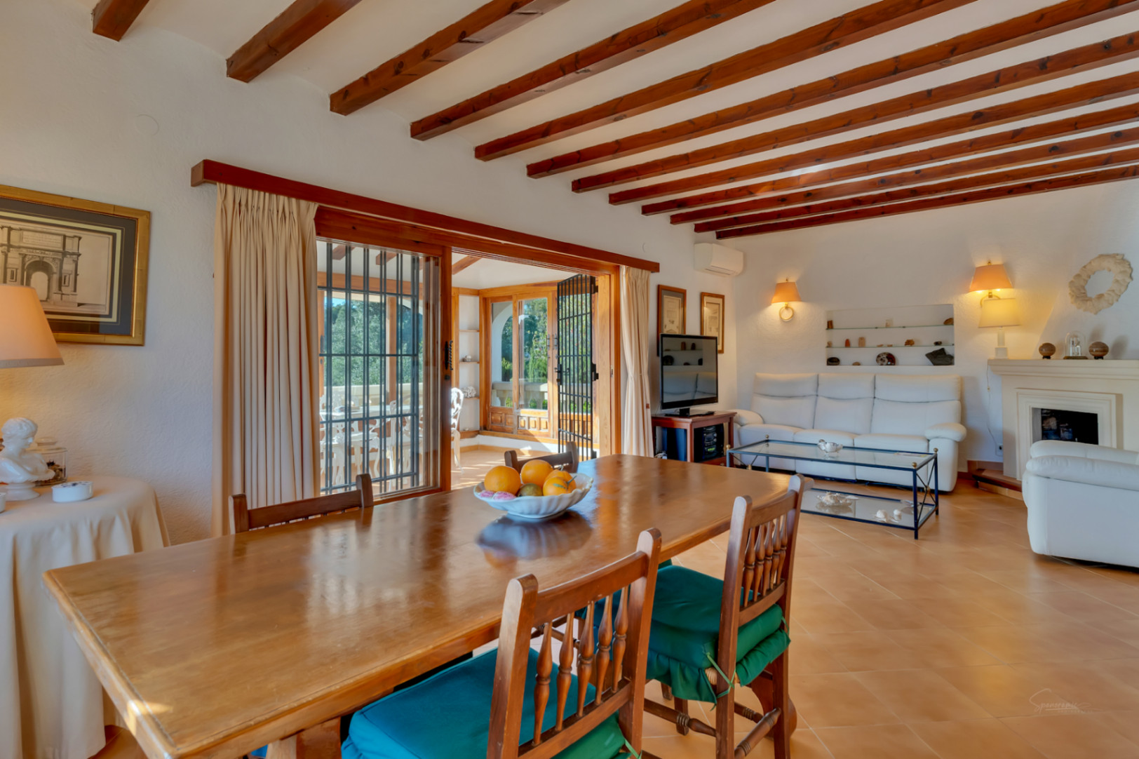 Mediterrane woon- en eetkamer met houten plafondbalken, terracotta vloeren en directe toegang tot een lichte, beglaasde naya.