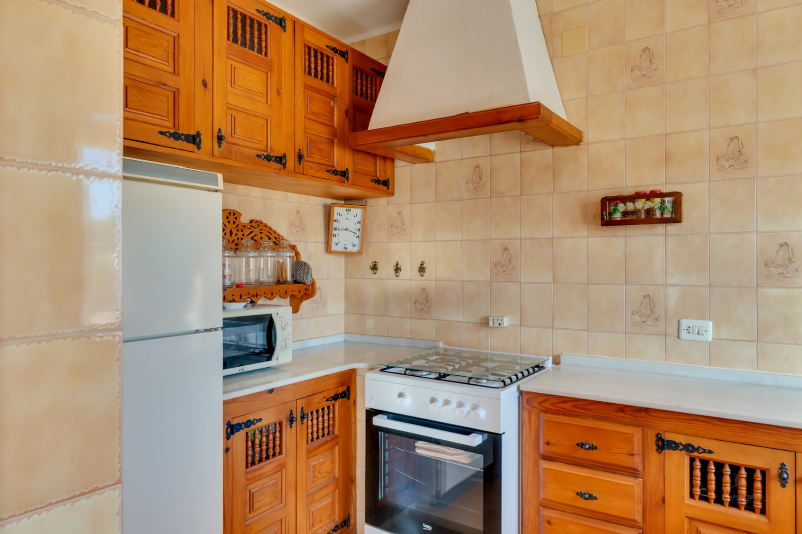 Traditionele keuken met gesneden houten kasten, smeedijzeren beslag en beige betegelde wanden met decoratieve motieven.