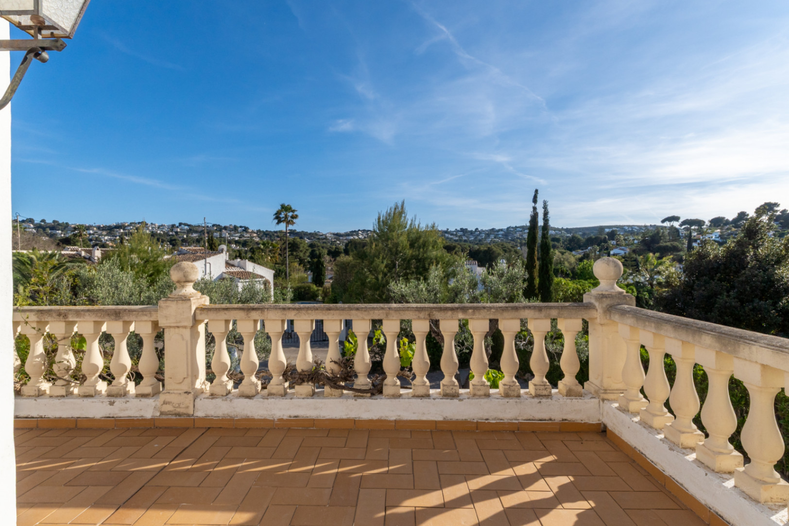 Verhoogd terras met terracotta tegelvloer en klassieke stenen balustrade, met uitzicht op de woonwijk en de mediterrane vegetatie van Jávea.