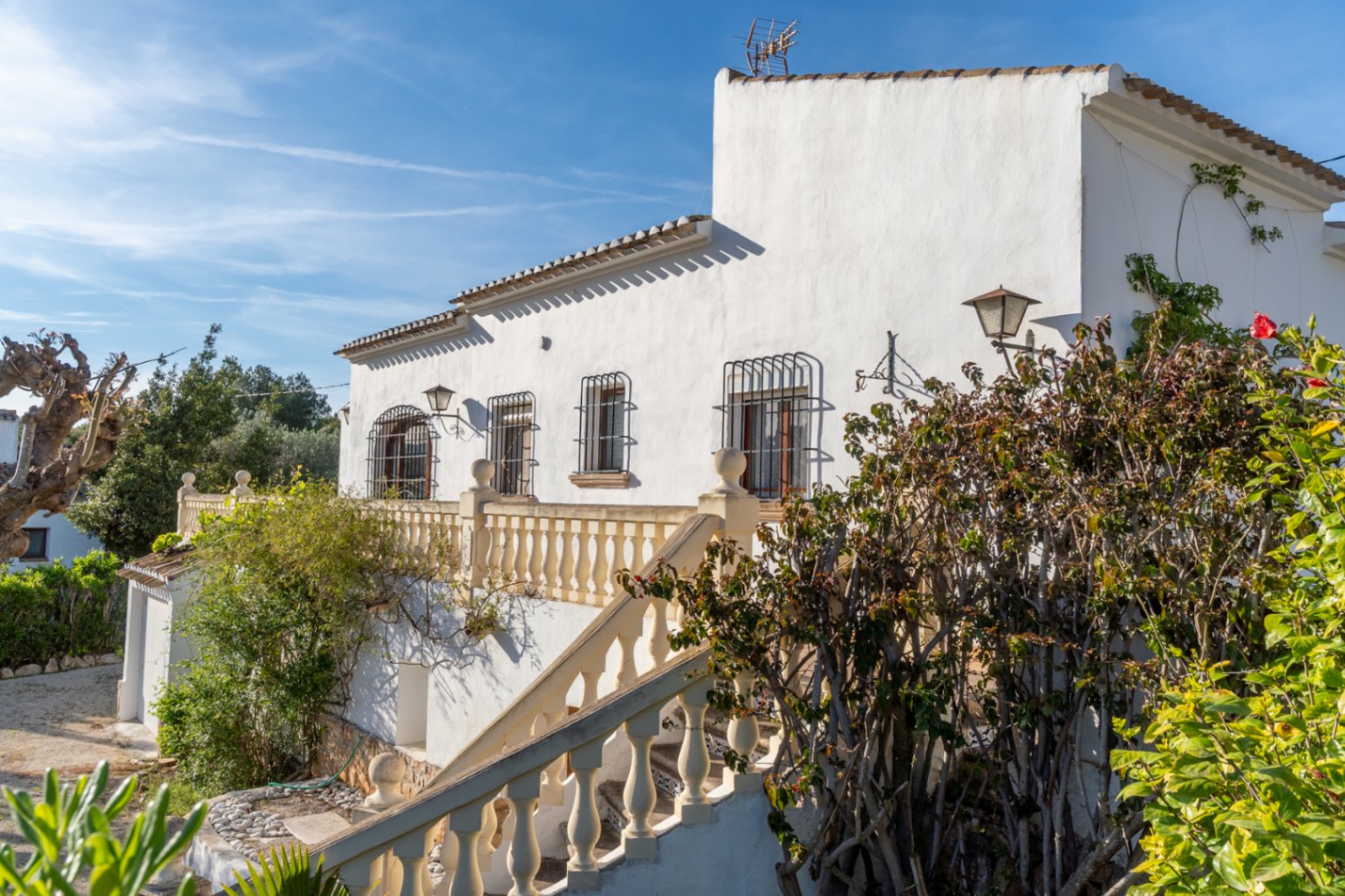 Witte mediterrane gevel met een klassieke balustrade, smeedijzeren tralies voor de ramen en een buitentrap die naar het hooftterras leidt.