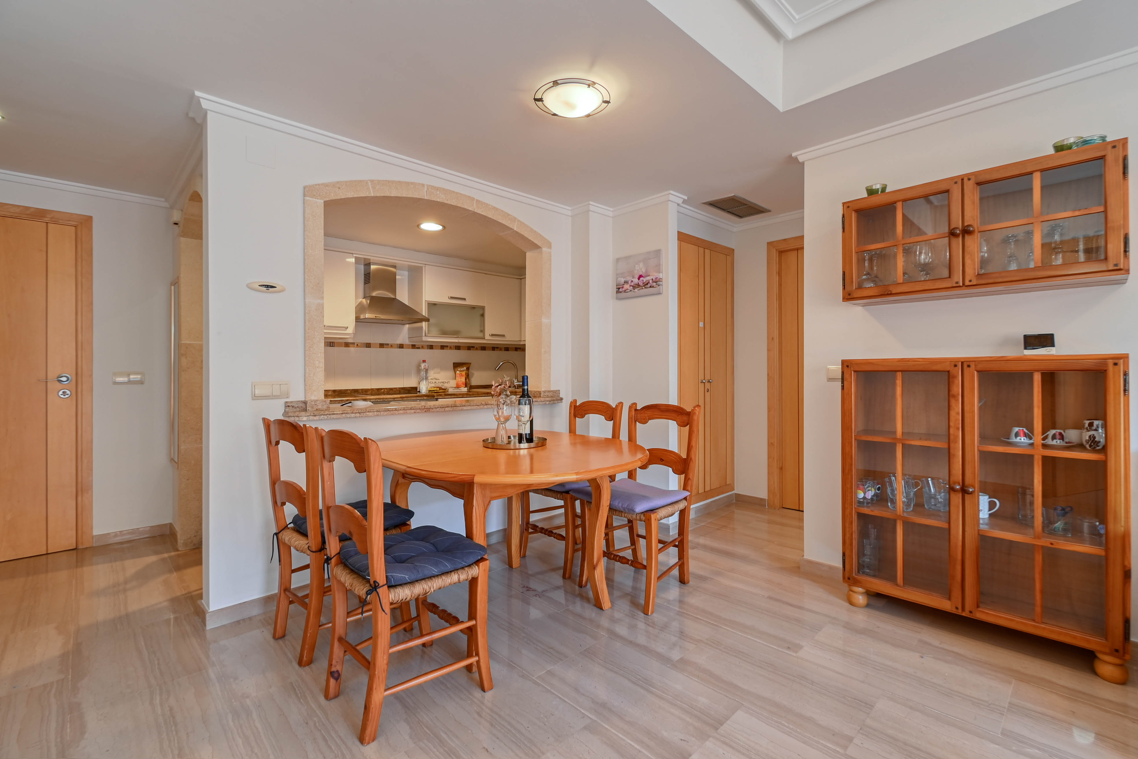 Eethoek met ronde houten tafel en stoelen, verbonden met de keuken via een stenen boog en voorzien van een gepolijste marmeren vloer.