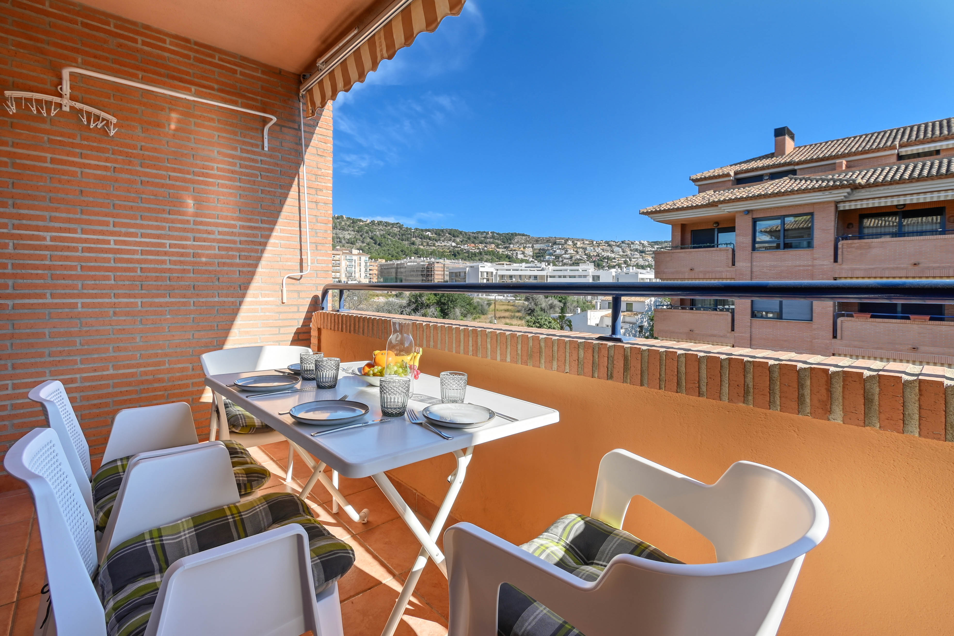 Privéterras met een buitentafel, gestreepte zonnewering en bakstenen muren. Het biedt een vrij uitzicht op de nabijgelegen heuvels en de woonwijk van Jávea.