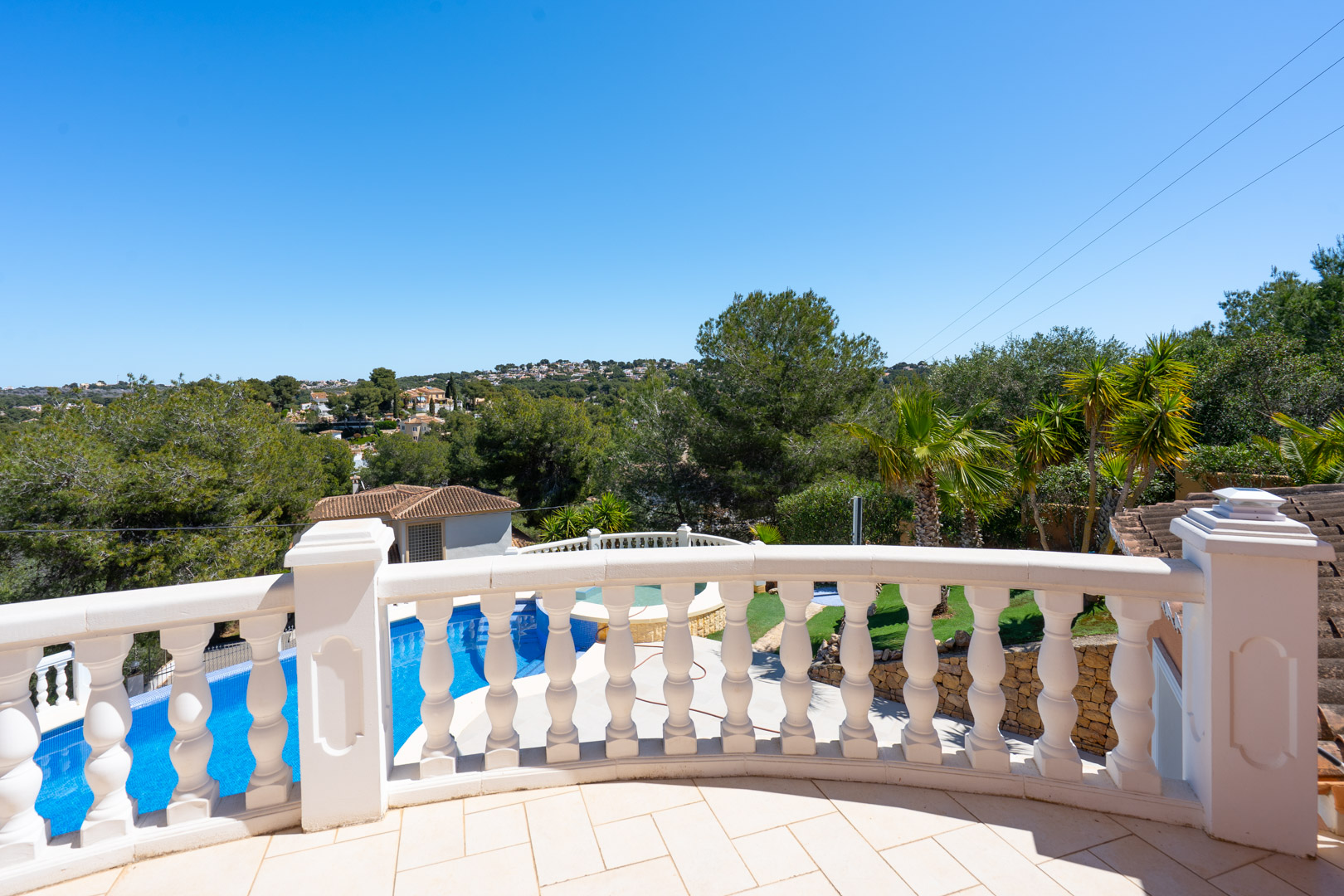 Bovenliggend terras met een klassieke witte balustrade en uitzicht op het privézwembad, de mediterrane tuin en de groene heuvels van Jávea.