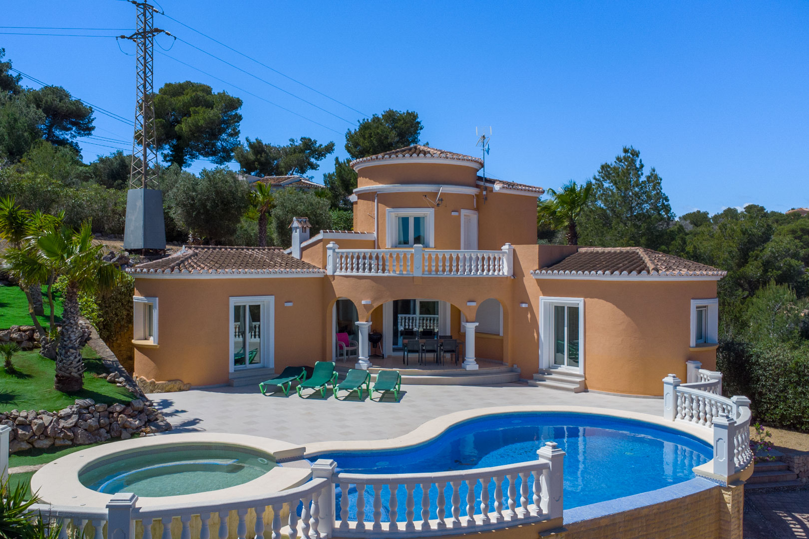 Exterieur van de villa met een niervormig zwembad, geïntegreerde jacuzzi en ruim zonneterras. De mediterrane gevel is voorzien van witte balustrades en een overdekt terras.