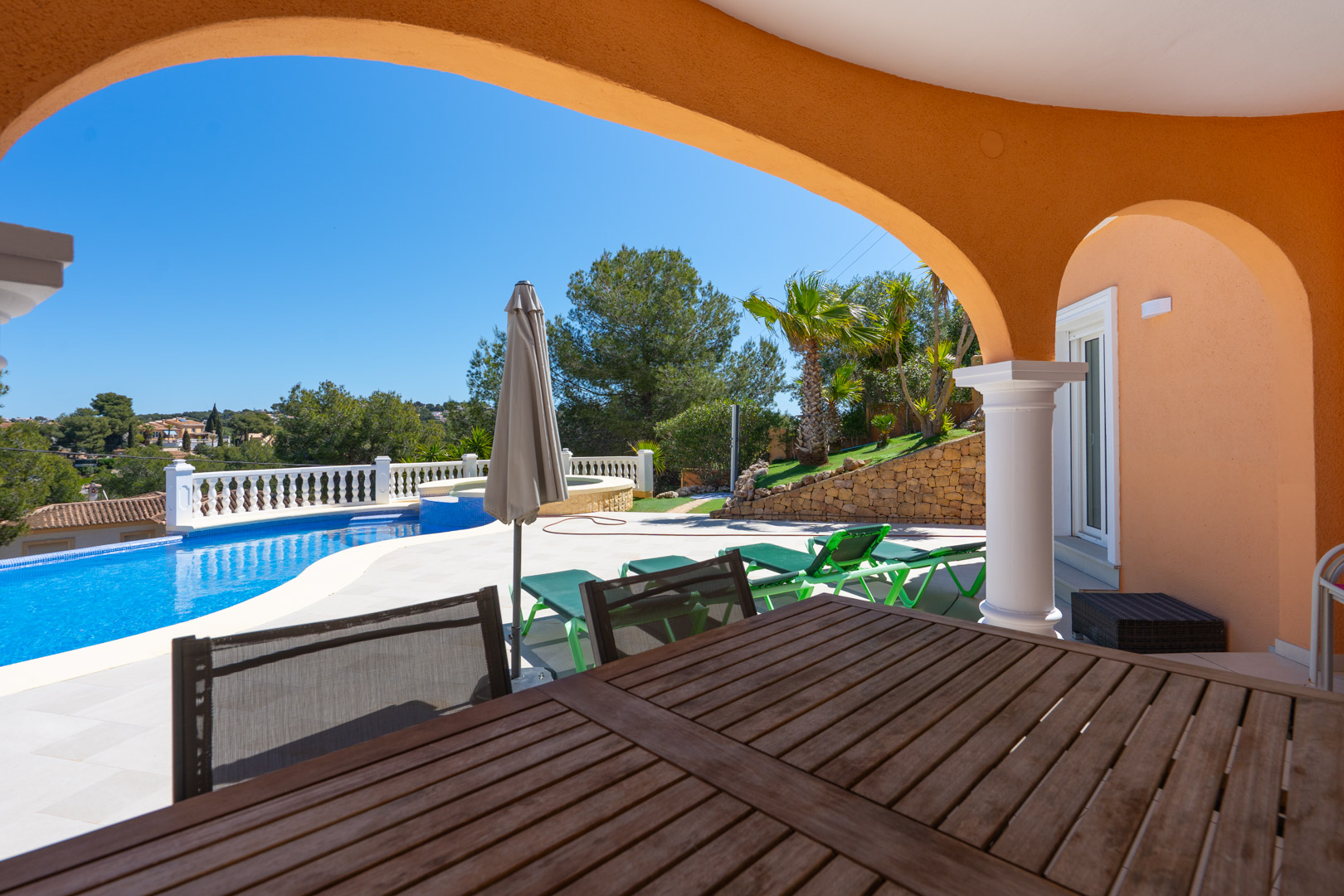 Overdekt terras met traditionele bogen en houten eethoek, uitkijkend op het privézwembad, de ligbedden en de mediterraanse tuin met natuurstenen muren.