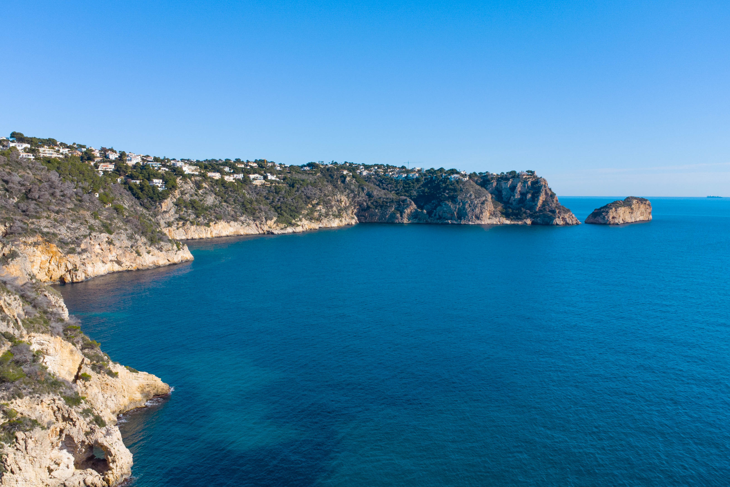 Panoramisch uitzicht op de kustlijn van Jávea met kalkstenen kliffen, de diepblauwe Middellandse Zee en villa's gelegen aan de rotsachtige kust.