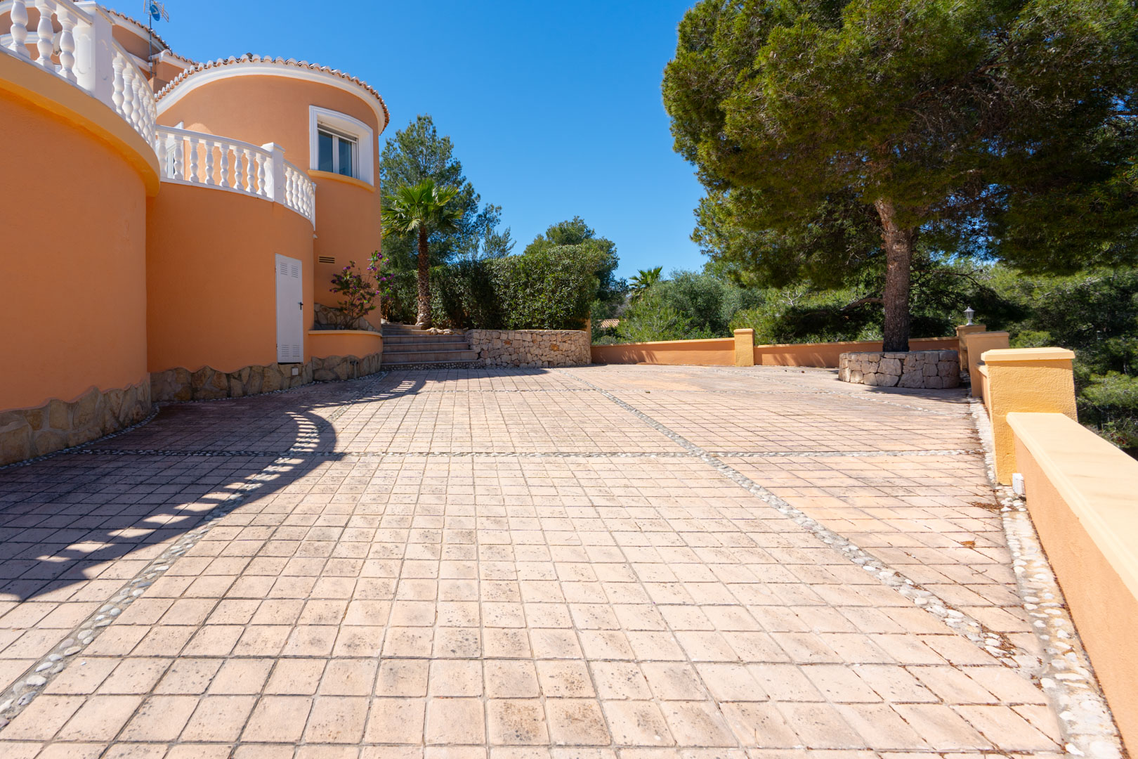 Ruim betegeld terras met decoratieve kiezelranden, gebogen terracotta muren met witte balustrades en volwassen mediterrane beplanting.