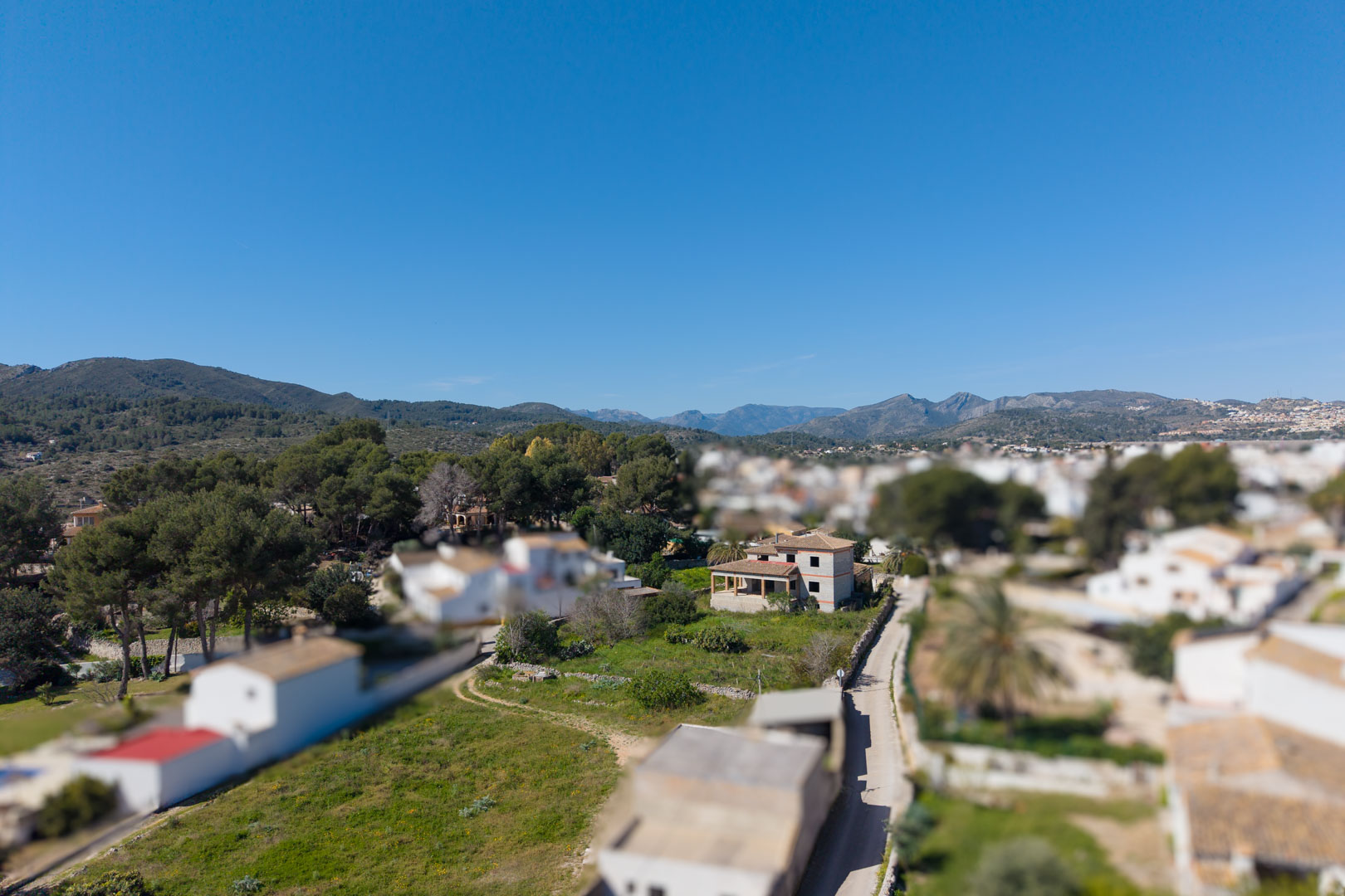 Luchtfoto van de woning in aanbouw op een royaal groen perceel in Gata de Gorgos, met een weids uitzicht op de bergen en het mediterrane landschap.