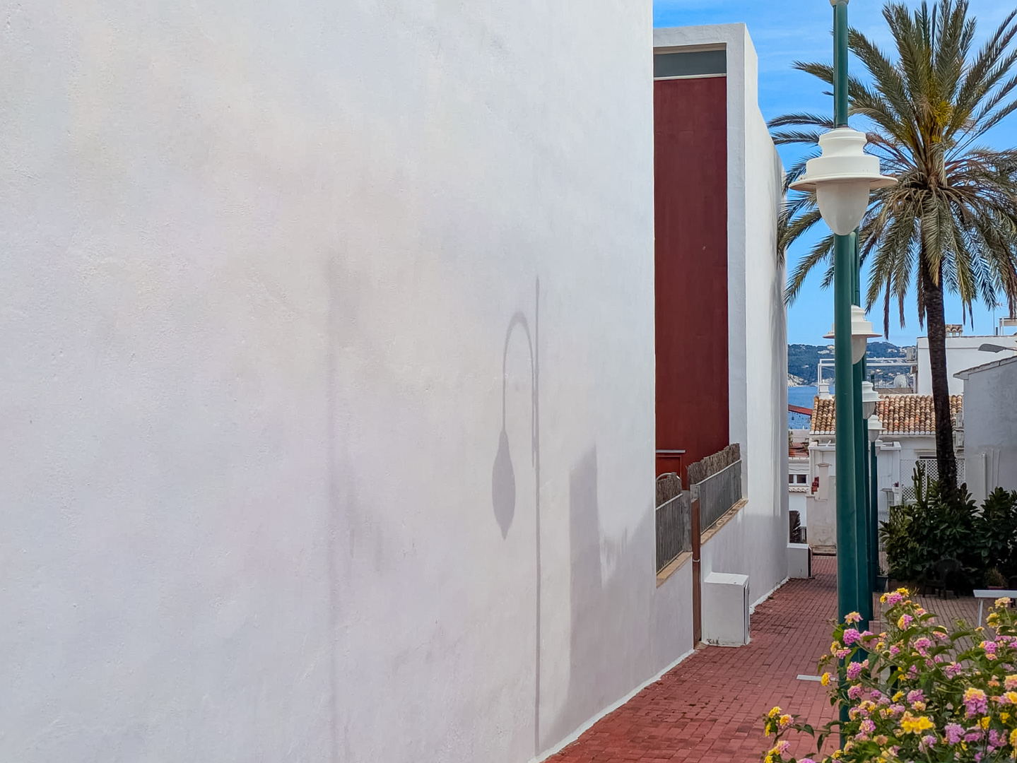 Exterieur van het gebouw met witte gevel en een bakstenen voetpad dat zijdelings uitzicht biedt op de zee en mediterrane beplanting.