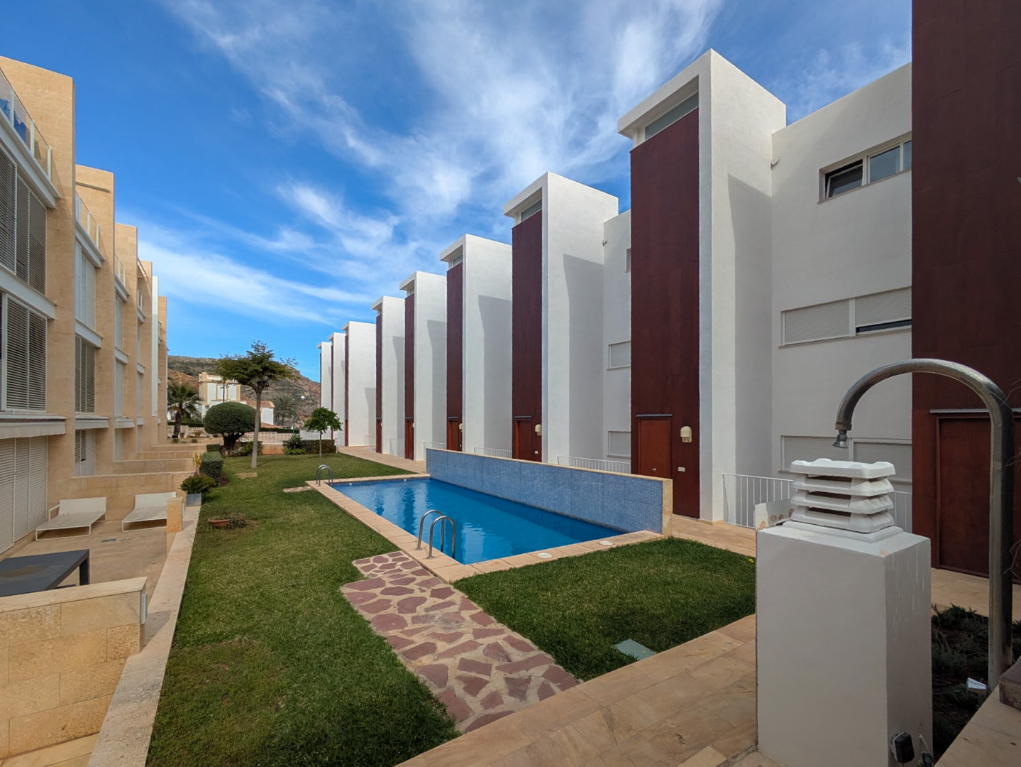 Gemeenschappelijke ruimte met een rechthoekig zwembad met blauwe mozaïektegels, gazons en stenen paden binnen een modern wooncomplex in Jávea.