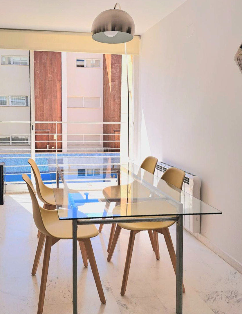 Lichte eethoek met glazen tafel, Scandinavische stoelen en marmeren vloer, met uitzicht op het gemeenschappelijke zwembad door de grote schuifpui.