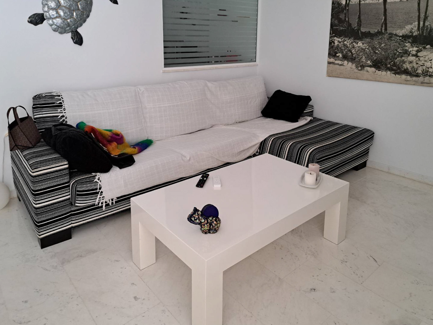 Woonkamer met marmeren vloer, een gestreepte hoekbank met witte hoezen en een minimalistische witte salontafel in een lichte omgeving.