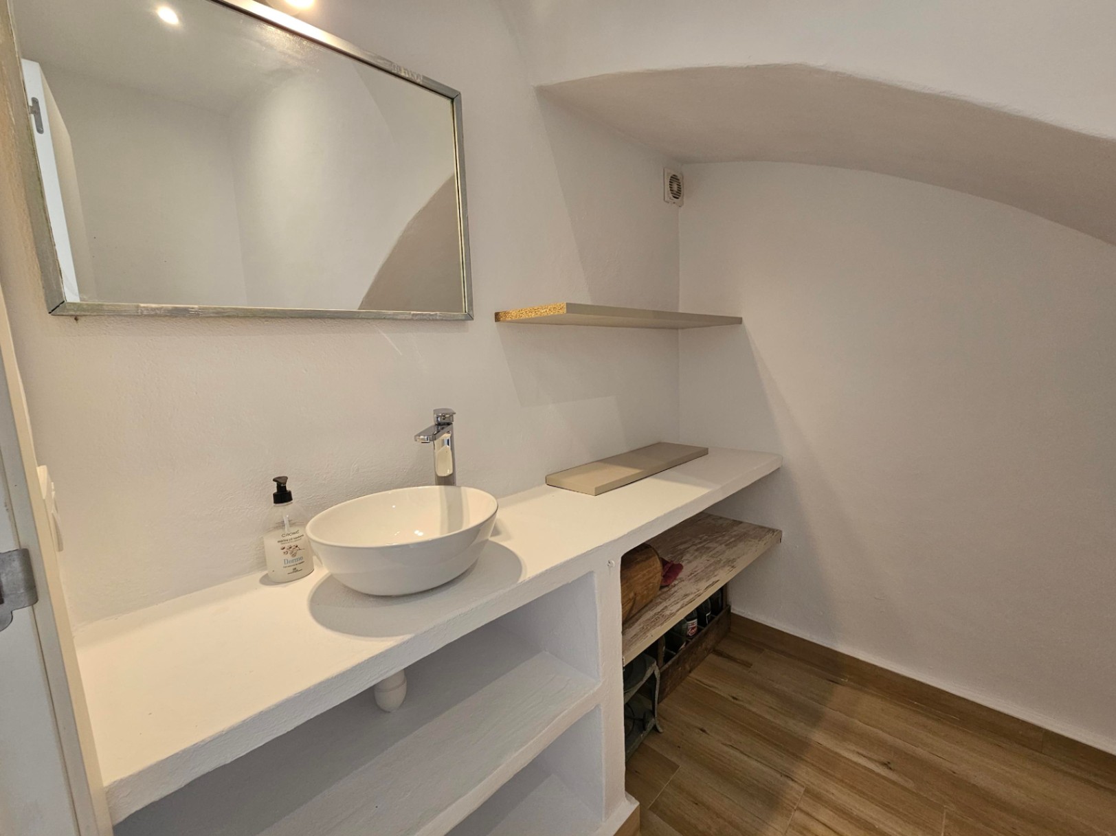 Gastentoilet met een witte opzetwastafel op een gemetseld blad, ingebouwde schappen, keramische parketvloer en een schuin plafond onder de trap.