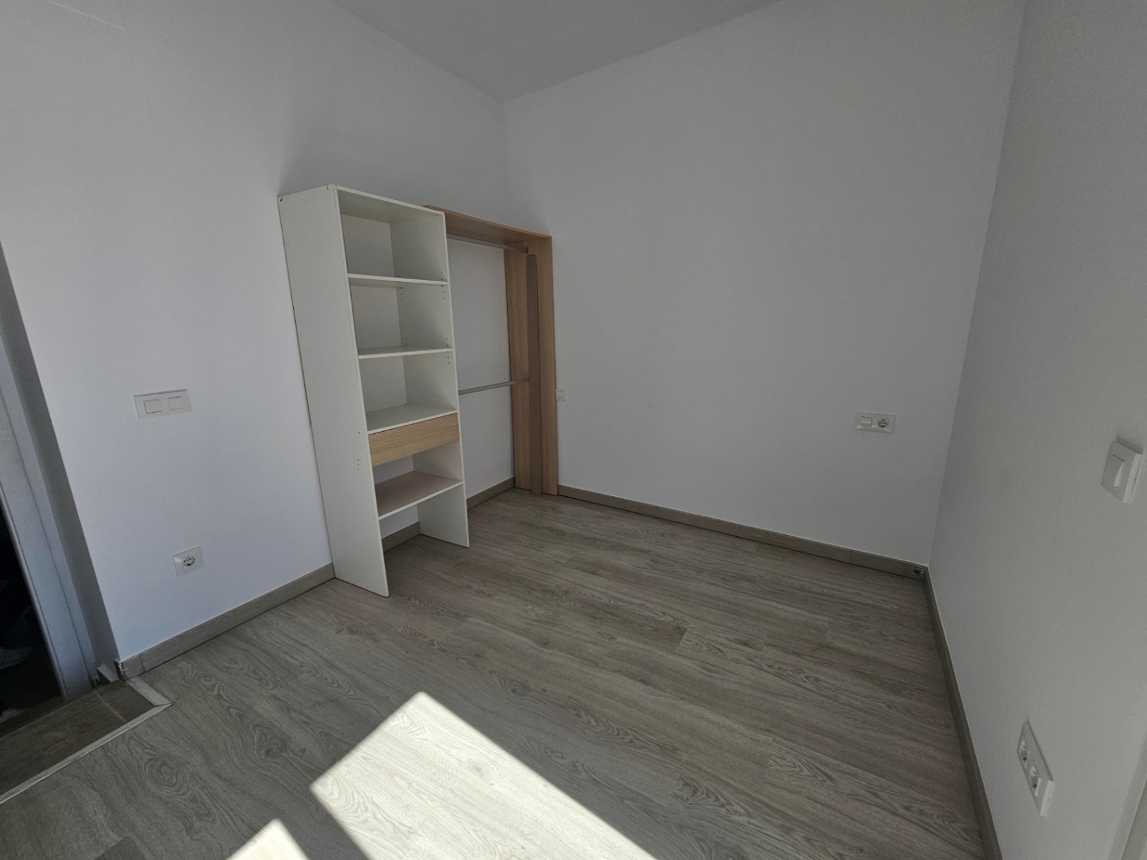 Lichte kamer met een lichte laminaatvloer, witte muren en een praktische open kledingkast met planken en hanggedeelte.