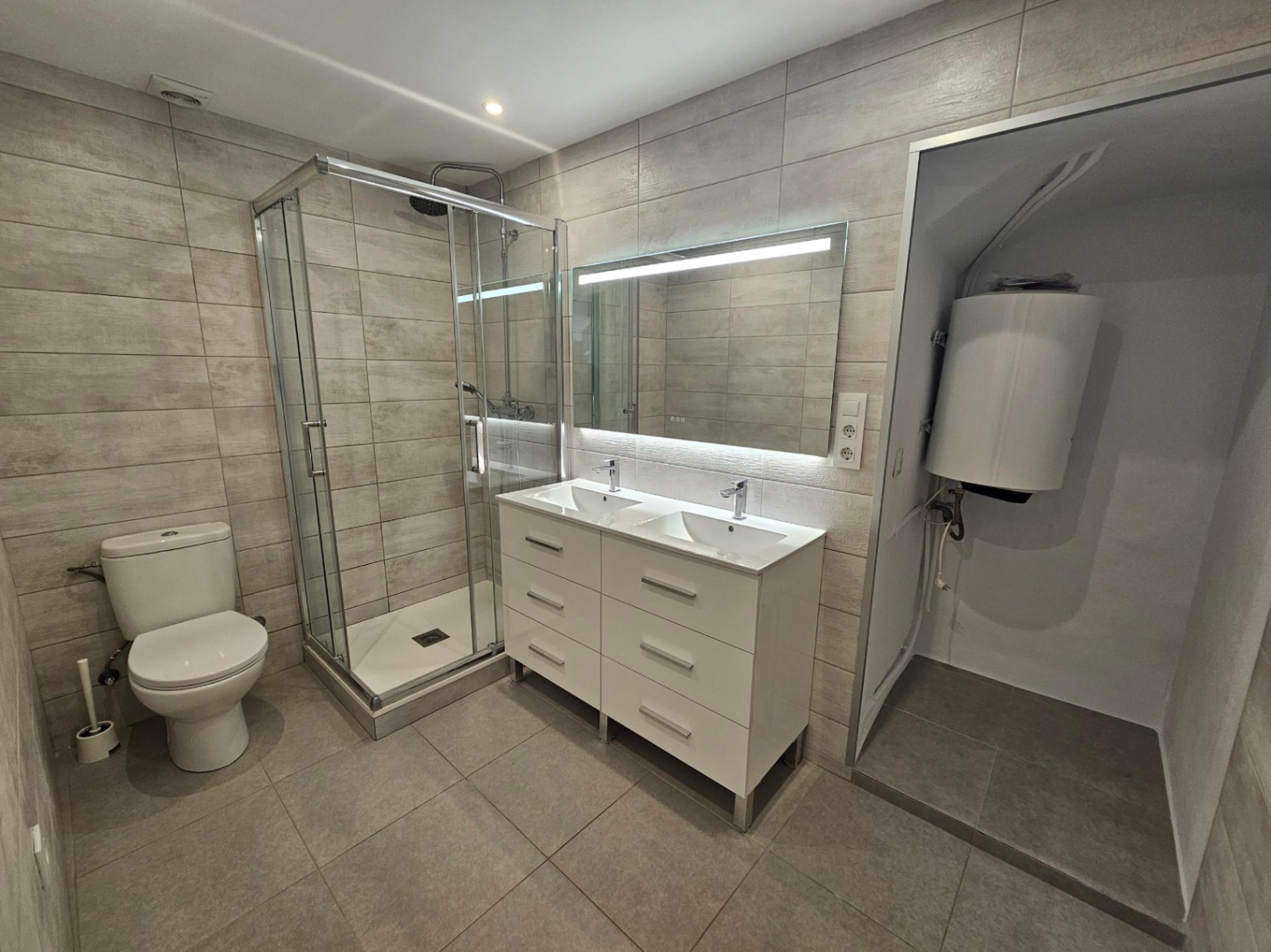 Moderne badkamer met glazen douchecabine, wit dubbel wastafelmeubel, verlichte spiegel en wandtegels met een natuurlijke steenlook.