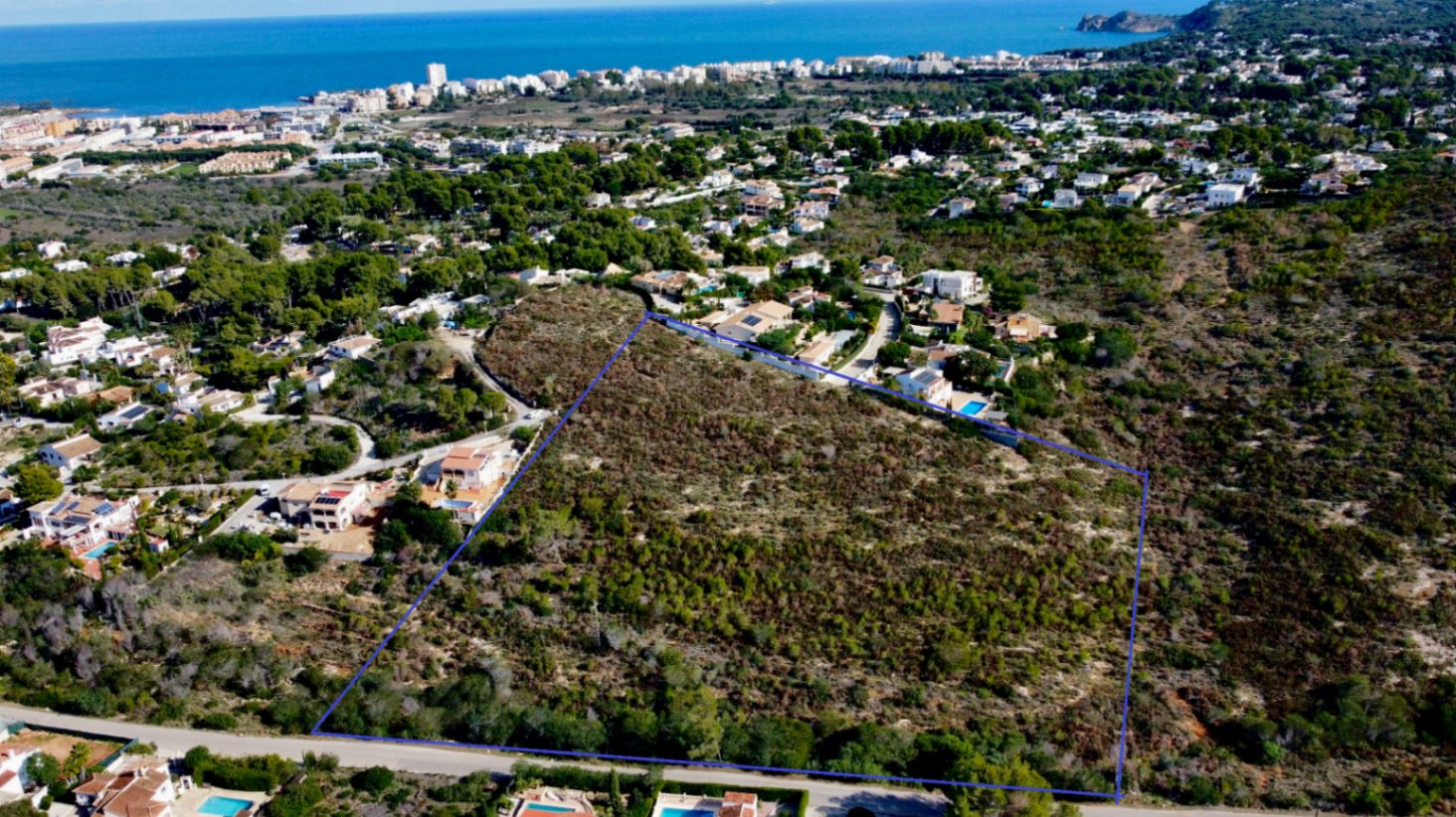 Luchtfoto van het grote perceel in Jávea, blauw omlijnd, die de omvang en strategische ligging toont met uitzicht op de Middellandse Zee en de kustlijn.