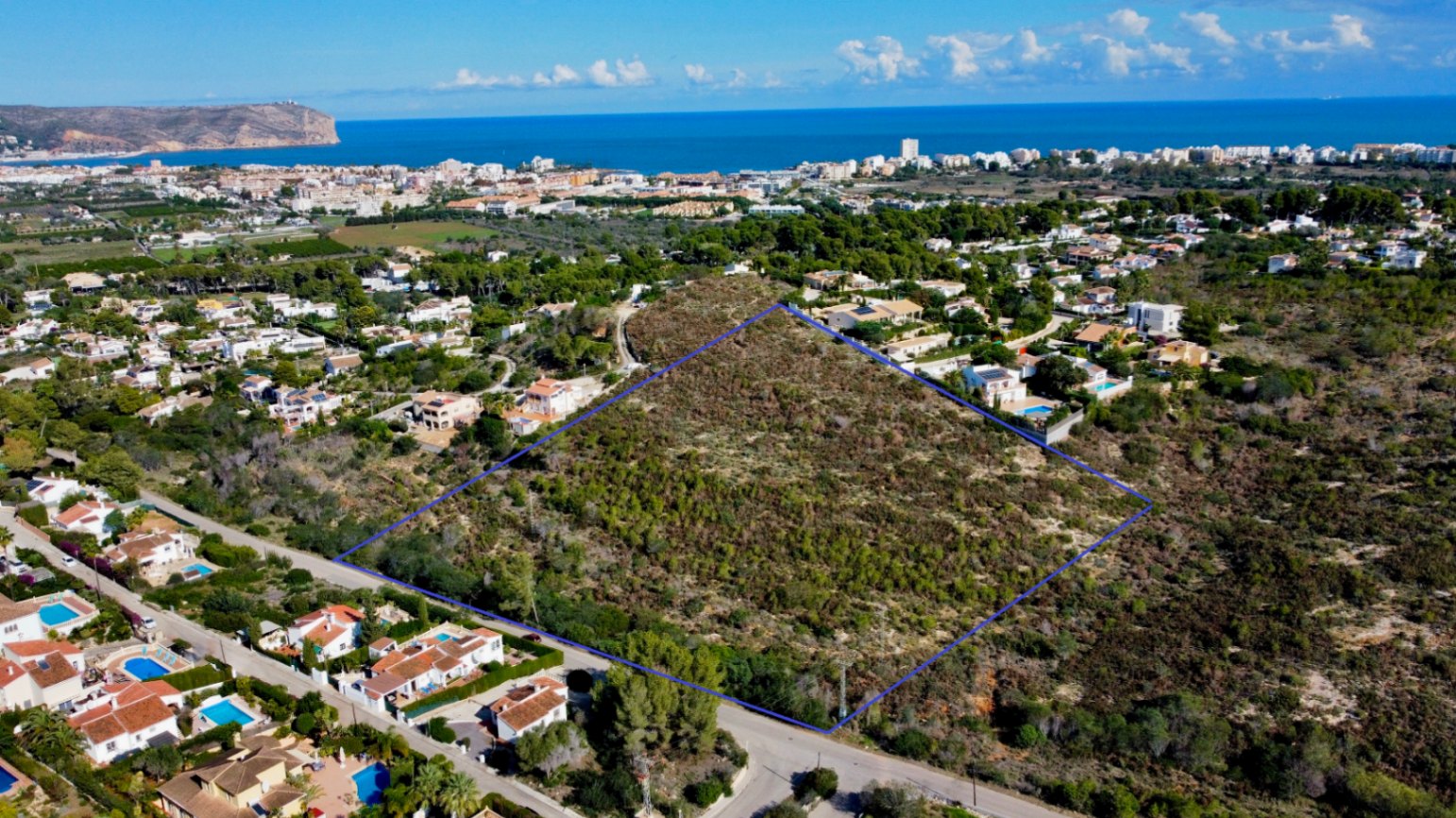 Luchtfoto van het perceel van 17.272 m² in Jávea, blauw omlijnd, gelegen nabij bestaande villa's met uitzicht op de Middellandse Zee.