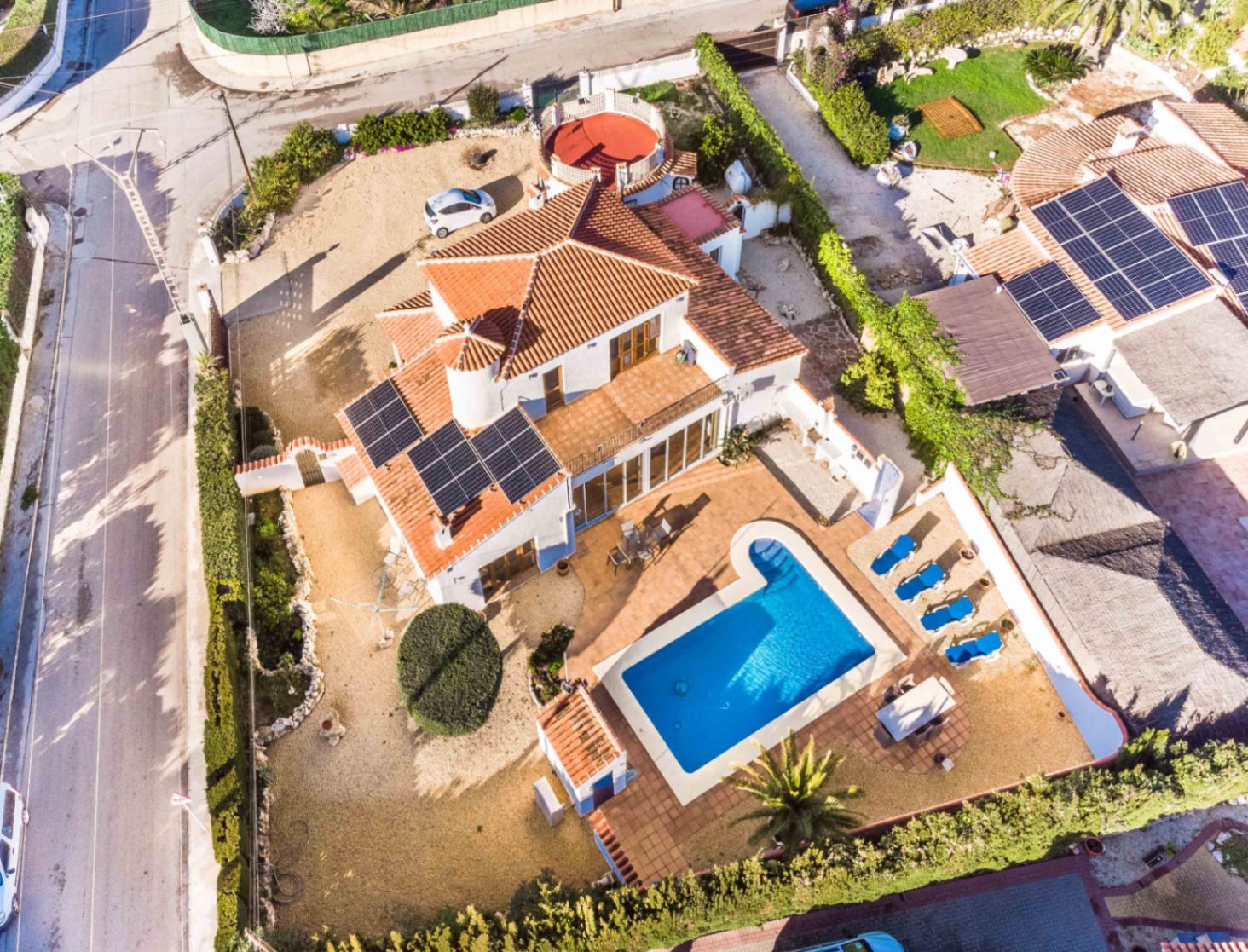Luchtfoto van de villa met privézwembad, zonneterras met ligstoelen, zonnepanelen op het dak en de ruime indeling van het hoekperceel.
