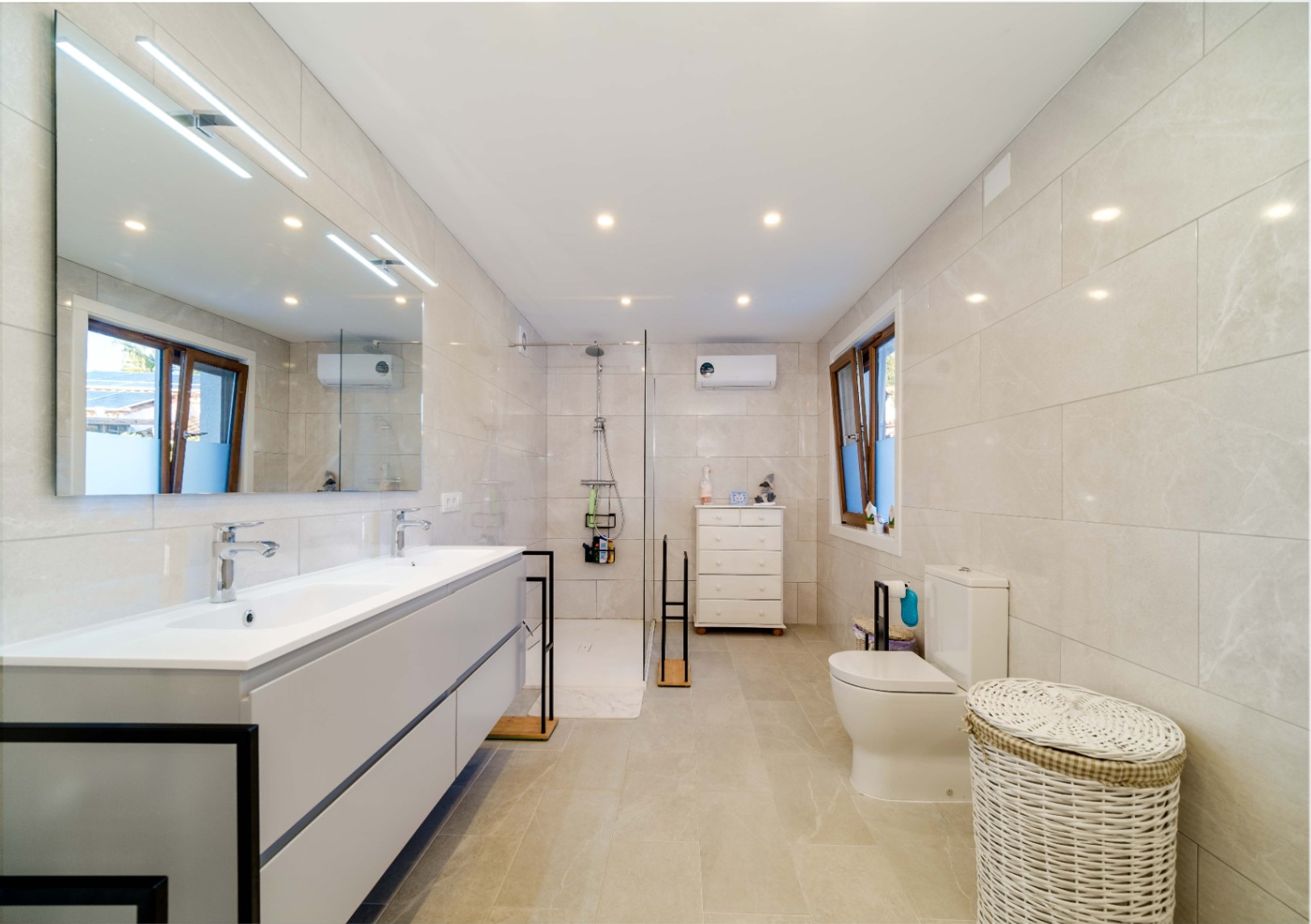 Moderne badkamer met dubbele wastafel, grijs zwevend meubel en grote verlichte spiegel. Voorzien van een inloopdouche, neutrale betegeling en inbouwspots.