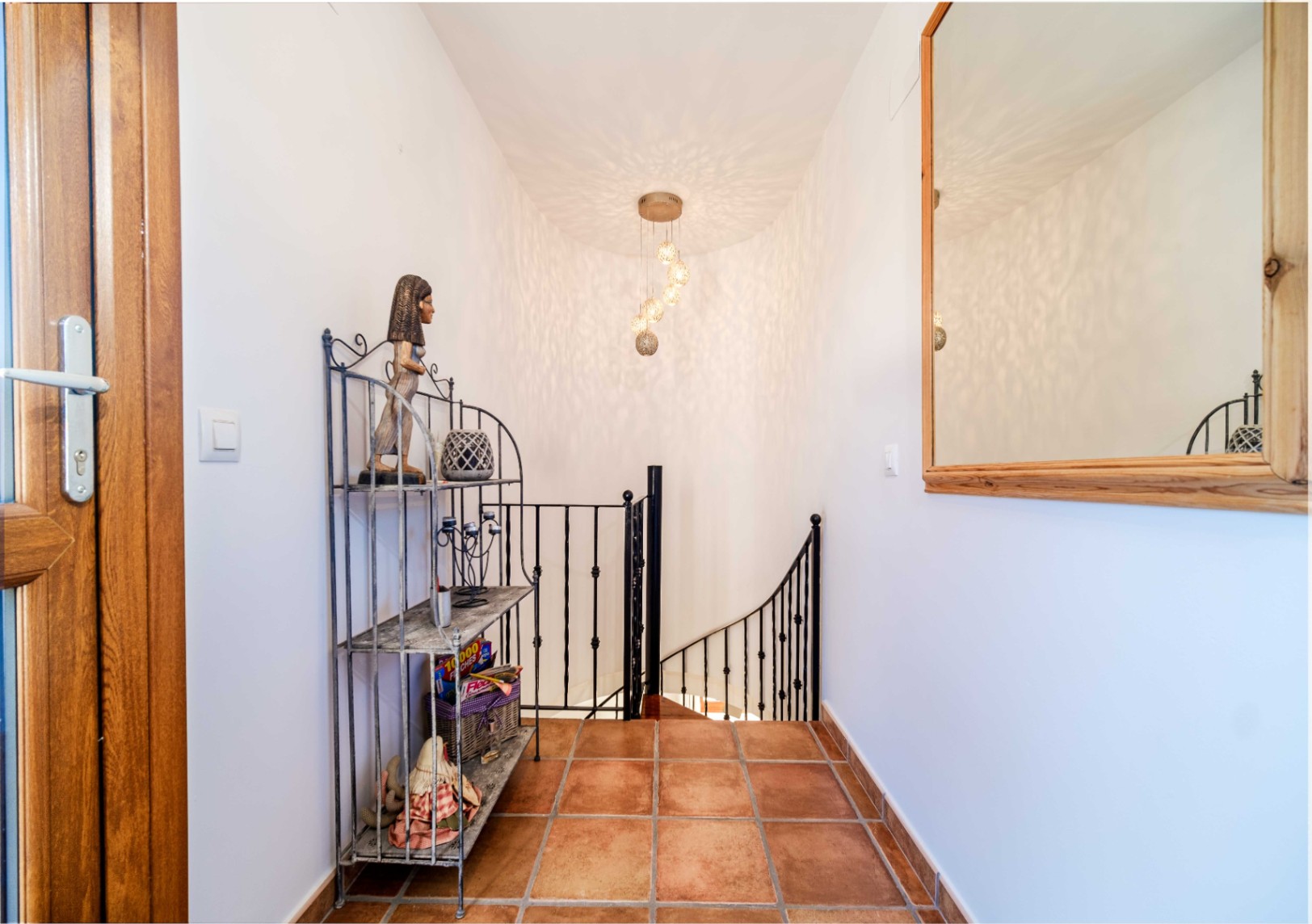 Overloop met terracotta tegelvloer, zwart smeedijzeren trapleuning en een gebogen trap verlicht door een moderne hanglamp.