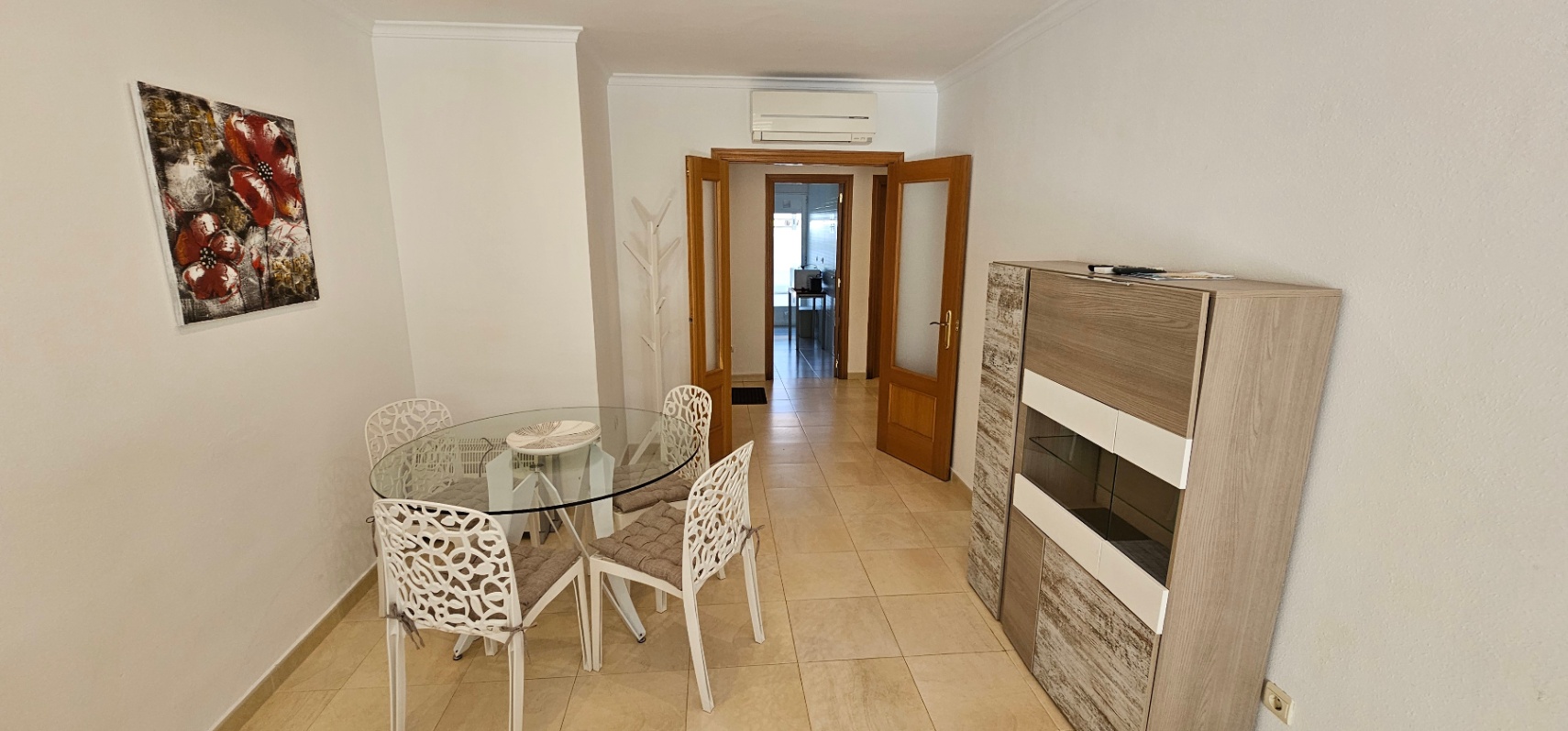Eethoek met een ronde glazen tafel, witte designstoelen en een modern dressoir, grenzend aan de hal via houten openslaande deuren.