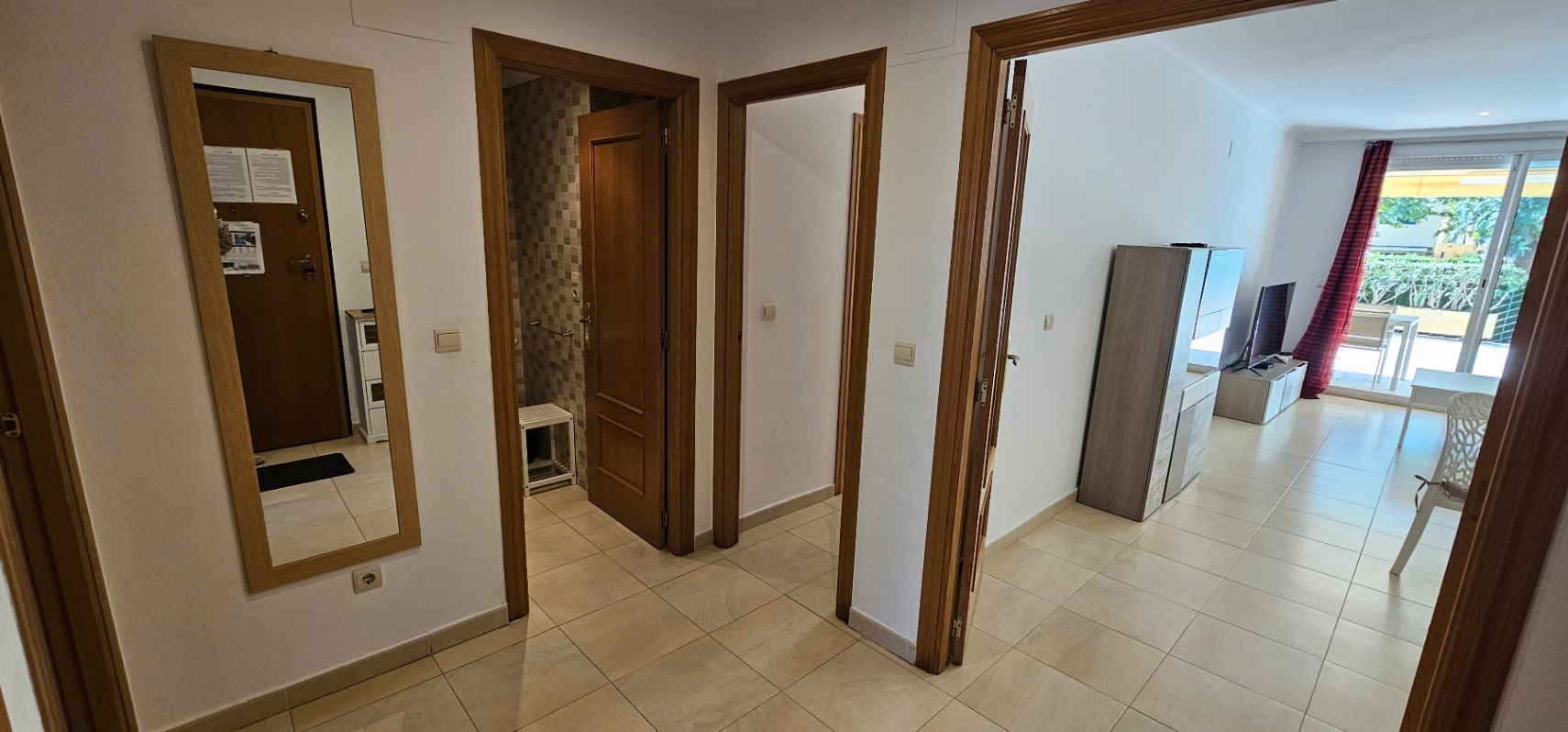 Entreehal met lichte tegelvloer en houten deurkozijnen, die toegang biedt tot een badkamer met mozaïektegels en de lichte woonkamer met terras.