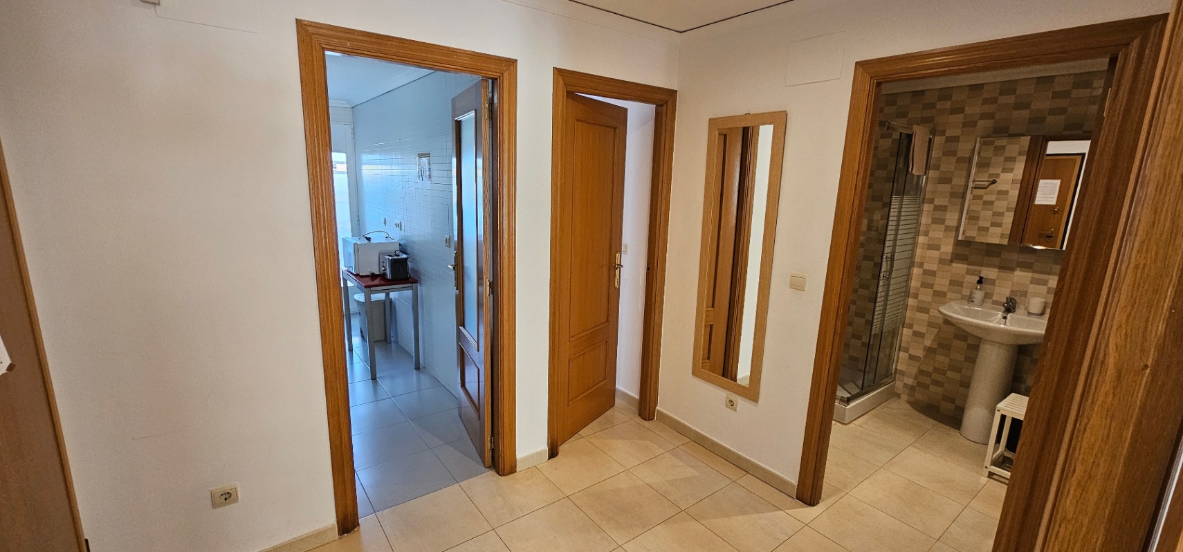 Hal met keramische vloertegels die toegang biedt tot de keuken, een slaapkamer en een badkamer met douchecabine en betegelde wanden.