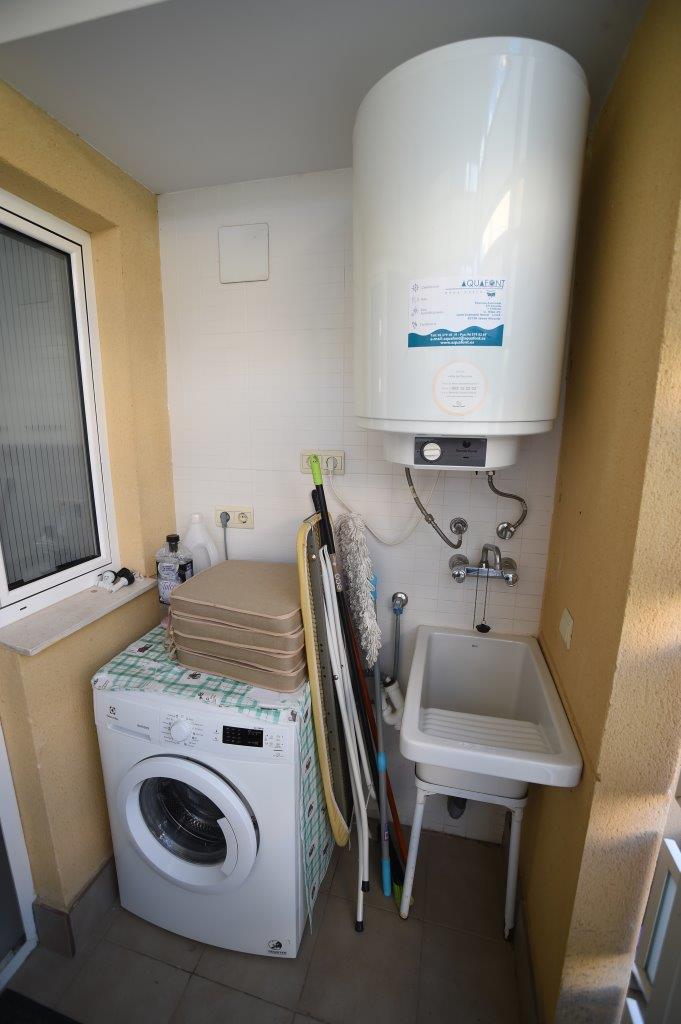 Overdekte bijkeuken voorzien van een wasmachine, een grote elektrische boiler en een praktische uitstortgootsteen voor huishoudelijk gebruik.