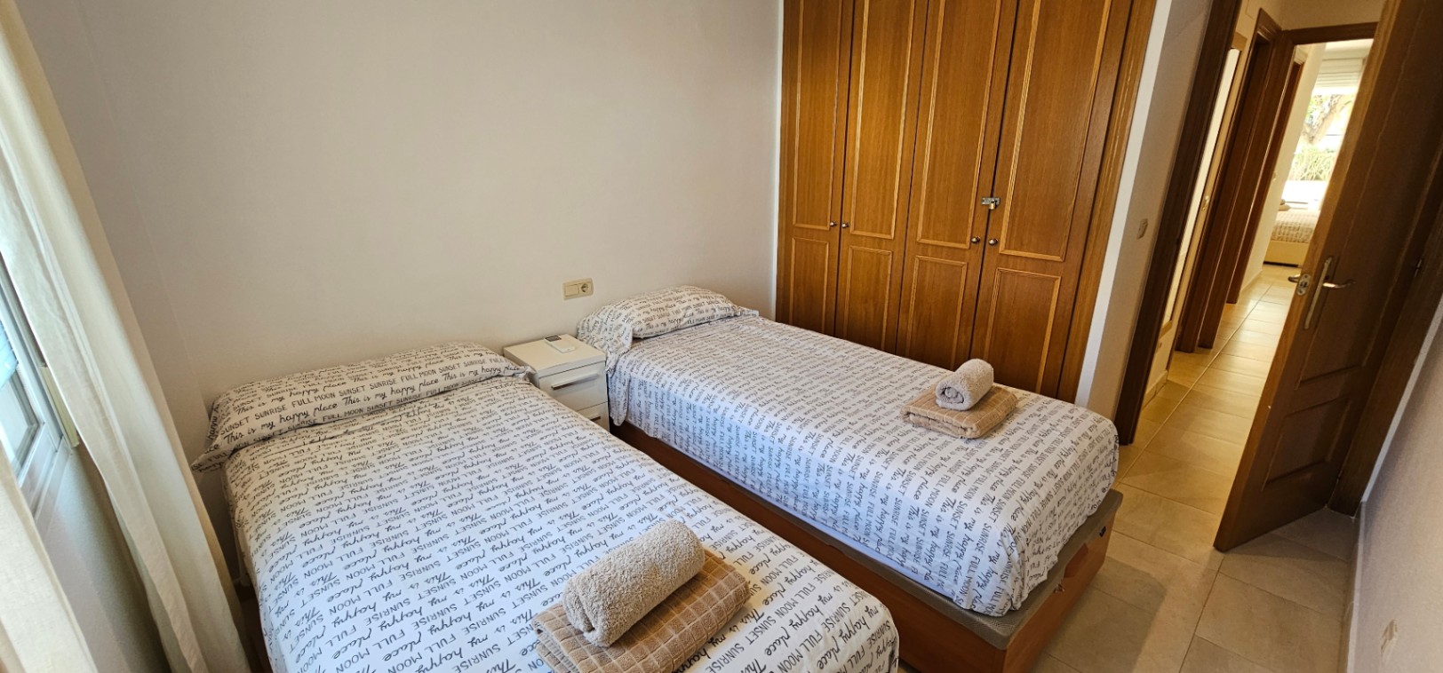 Slaapkamer met twee eenpersoonsbedden, een grote vierdeurs houten inbouwkast en een lichtgekleurde keramische tegelvloer.