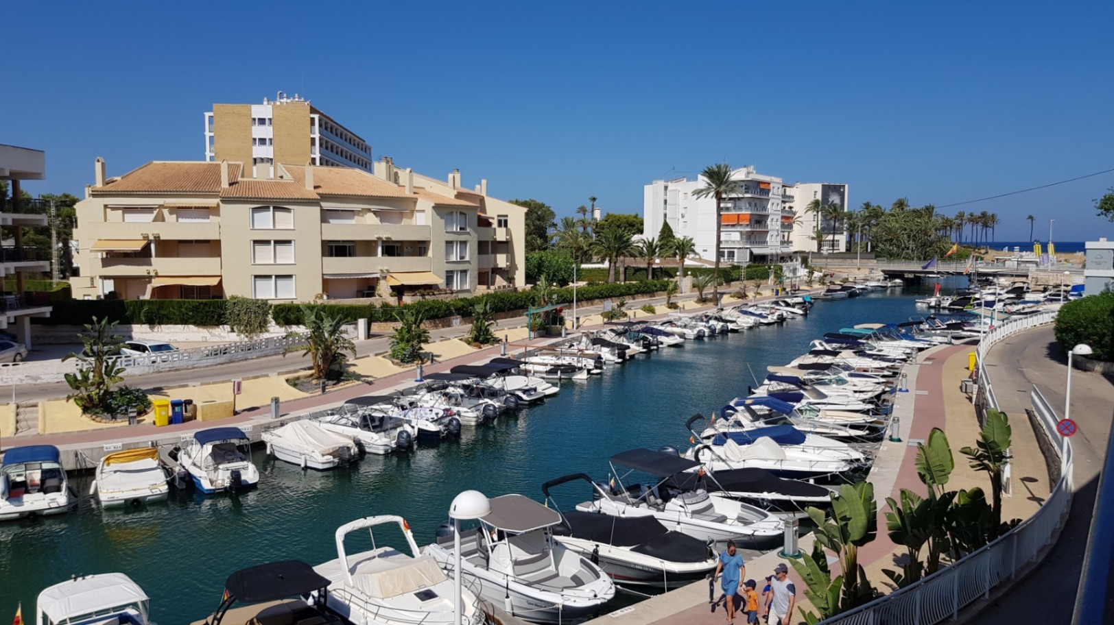 Panoramisch uitzicht vanaf het terras op het kanaal van de jachthaven, met aangemeerde pleziervaartuigen en woongebouwen onder een helderblauwe hemel in Jávea.