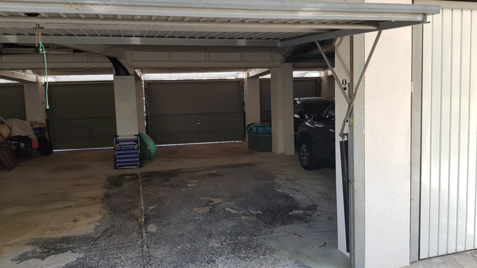 Privé overdekte garage met betonnen vloer en beveiligde metalen kanteldeuren, voor beschermd parkeren binnen het appartementencomplex.
