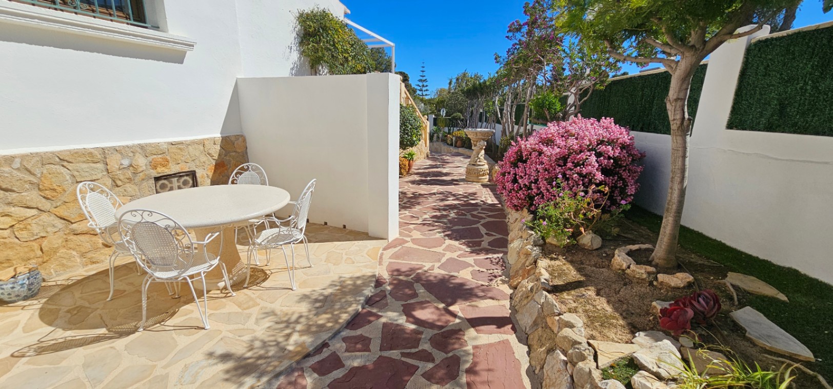 Buitenterras met natuurstenen bestrating, wit smeedijzeren meubilair en een mediterrane tuin met bloeiende struiken en stenen borders.