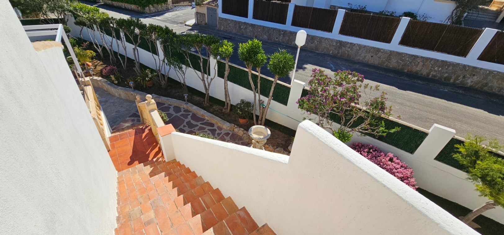 Buitentrap met terracotta tegels die leidt naar een aangelegde tuin met natuurstenen paden, gesnoeide bomen en mediterrane beplanting.