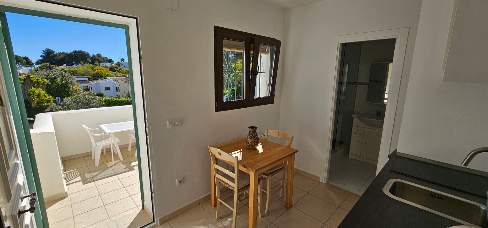 Eethoek met houten tafel, directe toegang tot het terras en zicht op de aangrenzende badkamer en het aanrecht.