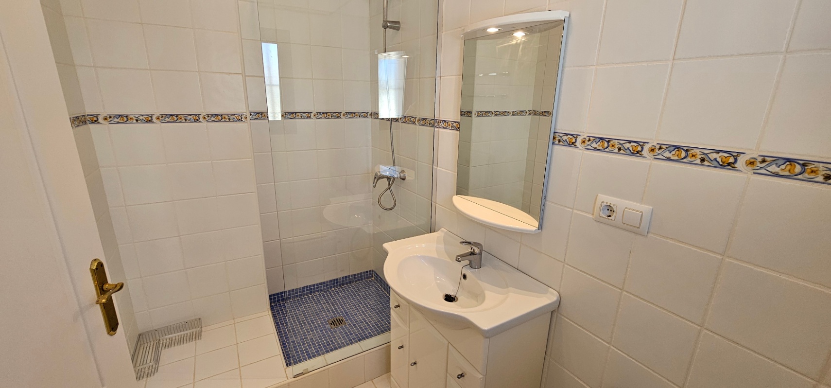 Functionele badkamer met inloopdouche voorzien van blauwe mozaïektegels, glazen wand, wit wastafelmeubel en verlichte spiegel.