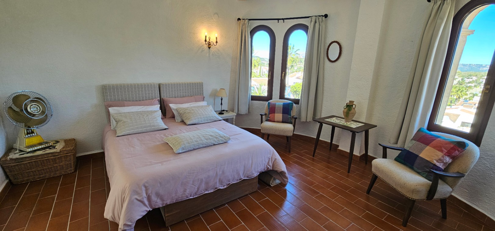 Lichte slaapkamer met terracotta tegelvloer, traditionele boogvensters en een zithoek. De ruimte combineert rustieke charme met natuurlijk licht en uitzicht op de omgeving.