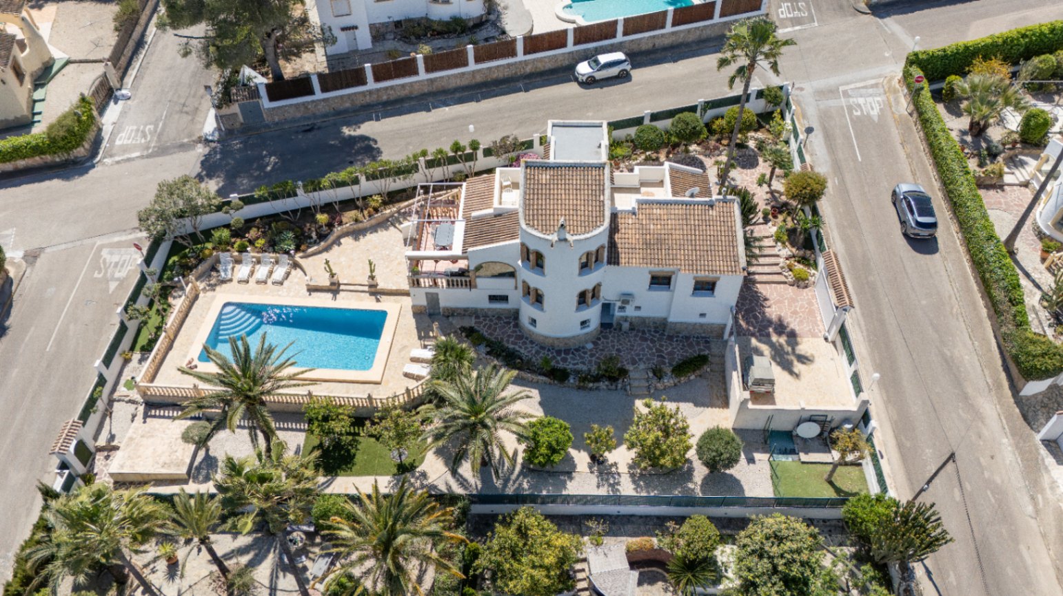 Luchtfoto van de villa op een hoekperceel, met een rechthoekig zwembad, een ronde toren en een mediterrane tuin met volwassen palmbomen.
