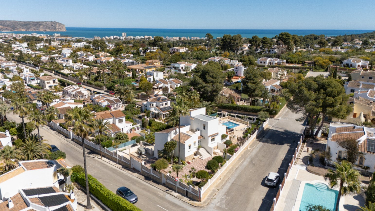 Luchtfoto van de witte villa op een hoekperceel in Pinosol, Jávea. Zichtbaar zijn het privézwembad, de mediterrane tuin en het weidse uitzicht op de Middellandse Zee.