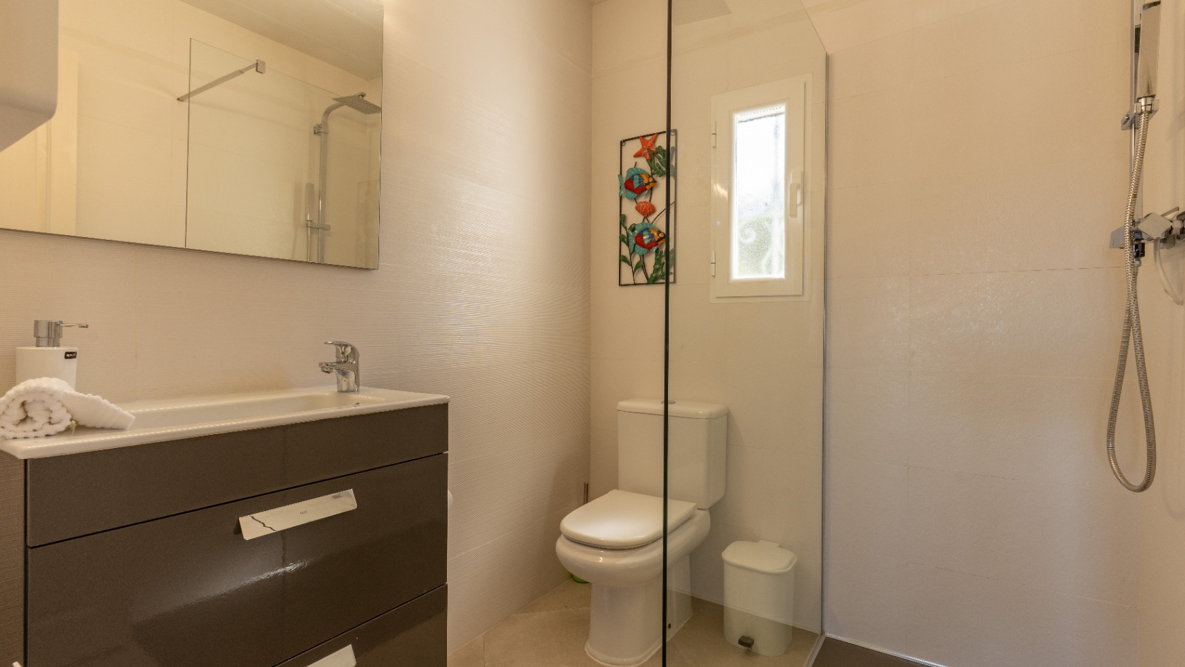 Moderne badkamer met een donkergrijs wastafelmeubel, glazen douchewand en neutrale crèmekleurige wandtegels met een subtiele textuur.