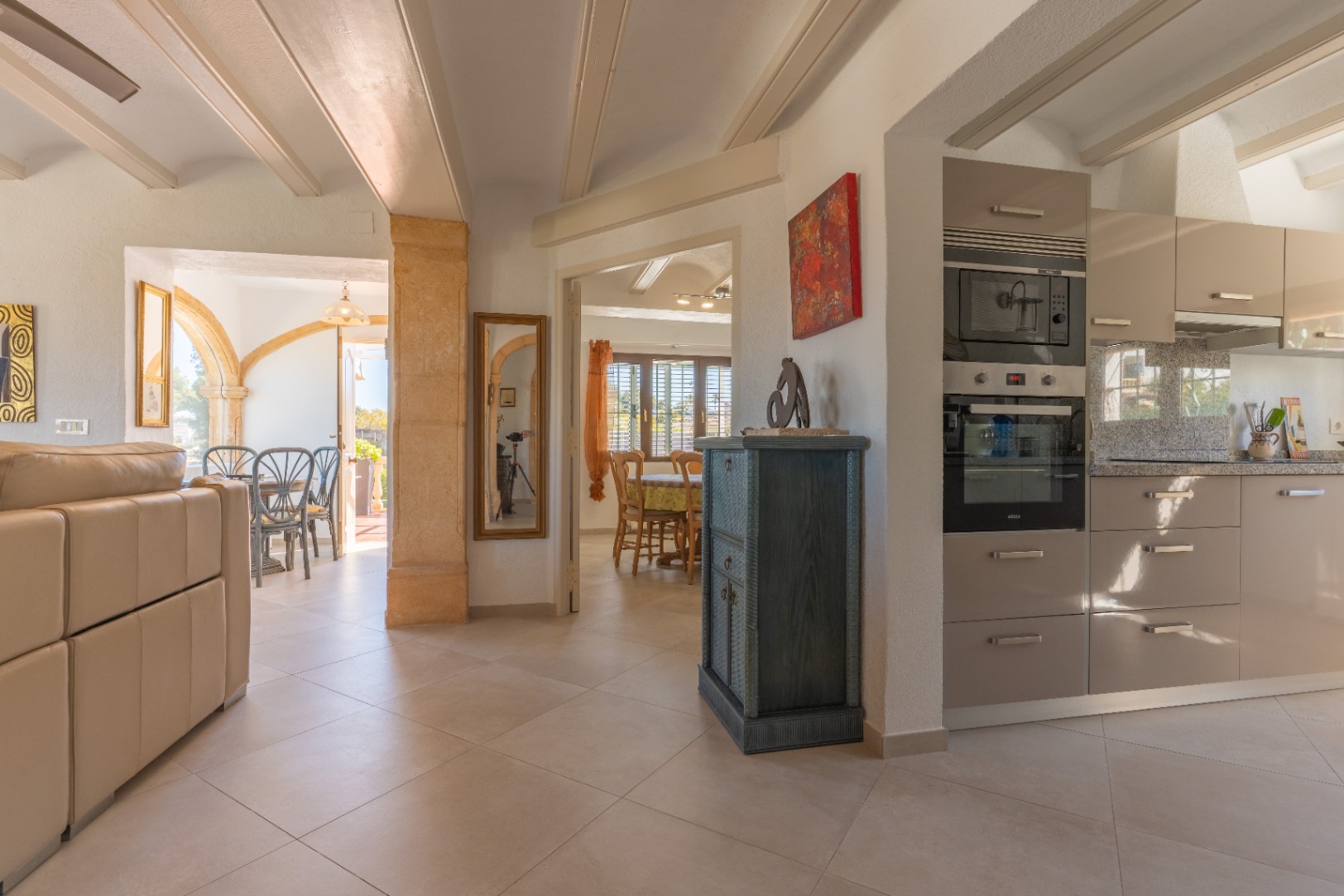 Open leefruimte met moderne keuken, balkenplafond en een karakteristieke Tosca stenen boog die de woonkamer verbindt met het aangrenzende terras.