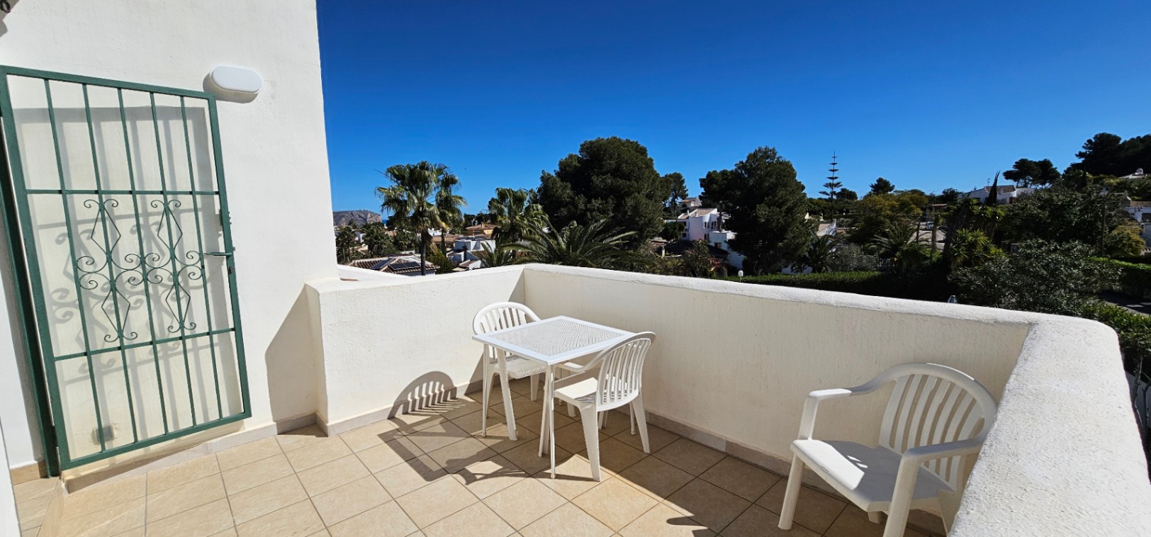 Open terras op de bovenverdieping met tegelvloer, wit buitenmeubilair en vrij uitzicht over de groene omgeving en naburige villa's in Pinosol.
